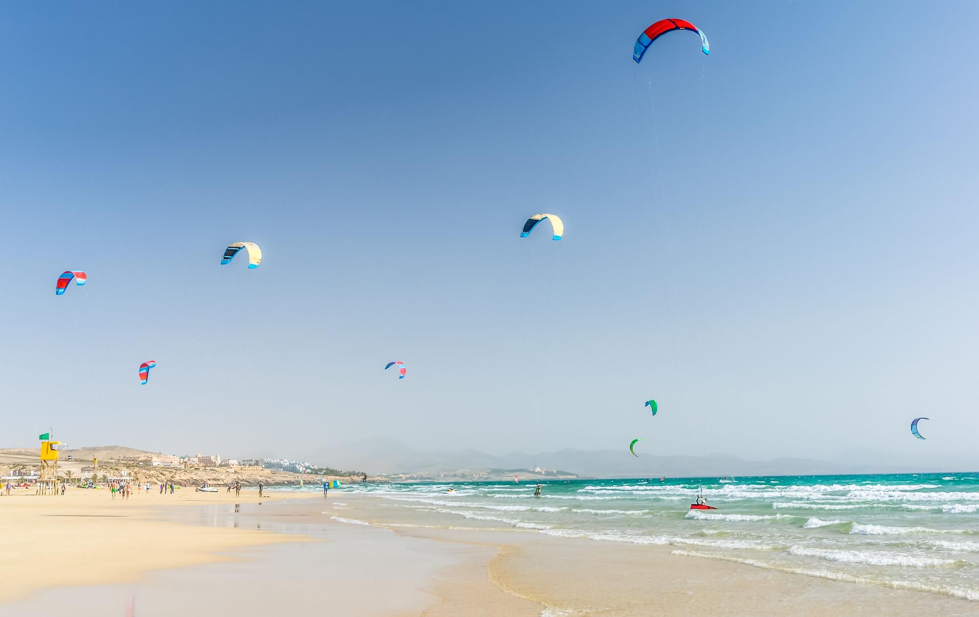 Im türkisgrünen Meer sind viele Kitesurfer zu sehen. Der Sand ist hell.