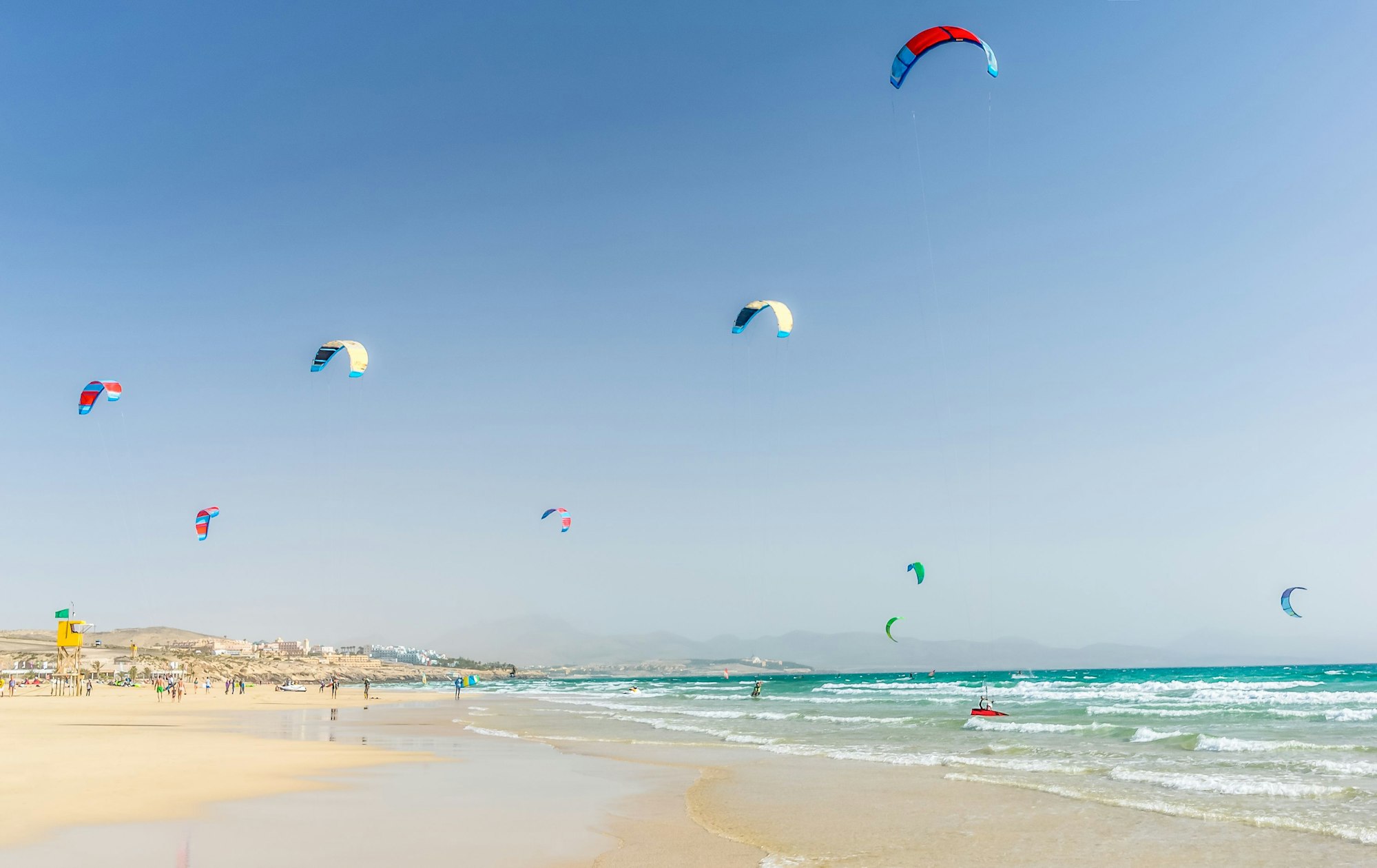 Im türkisgrünen Meer sind viele Kitesurfer zu sehen. Der Sand ist hell.
