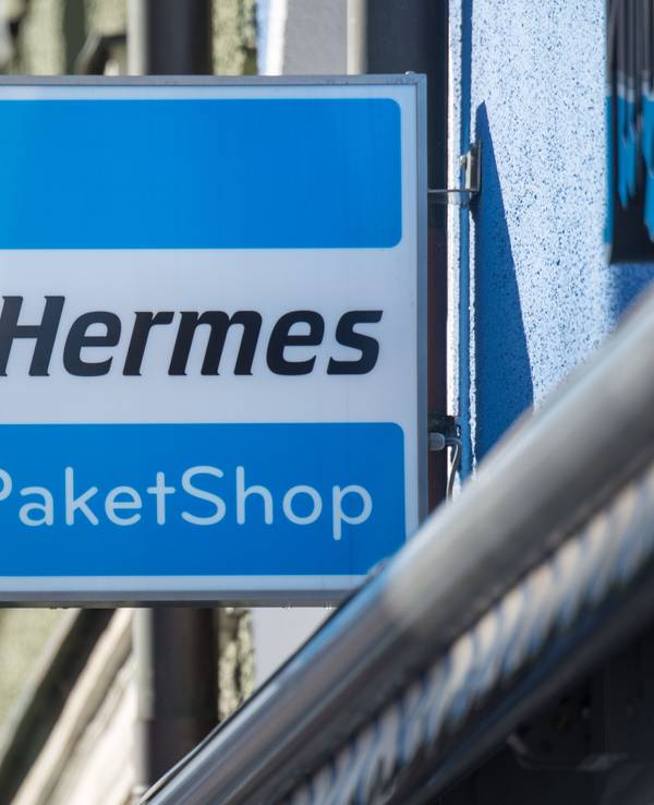 Ein Schild mit der Aufschrift „Hermes Paket Shop“ ist vor einem Geschäft angebracht.