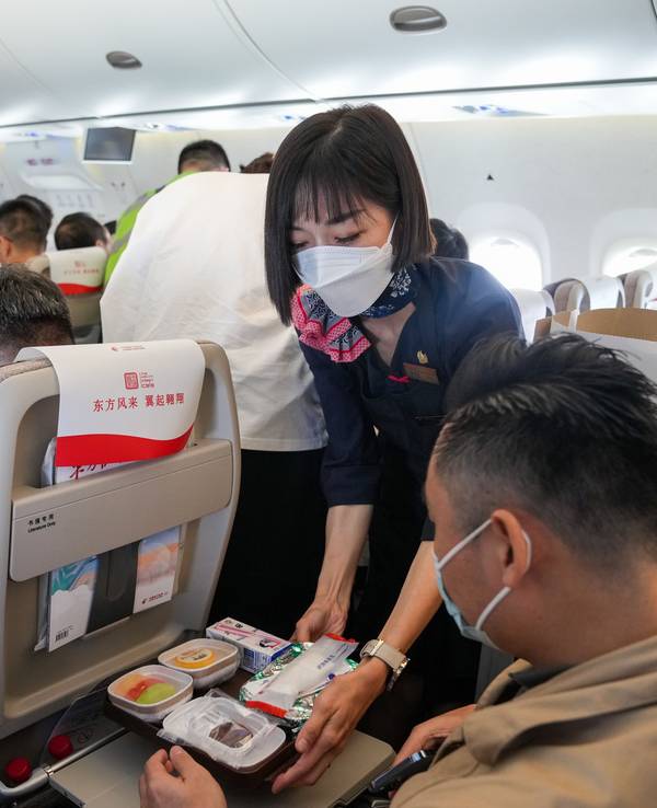 Eine Flugbegleiterin serviert einem Passagier an Bord eine Mahlzeit.