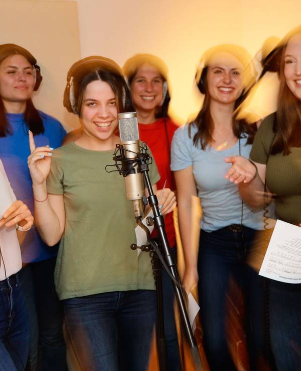 Sieben Sängerinnen vom Chor und der Chorleiter stehen im Studio und nehmen ein Lied auf.