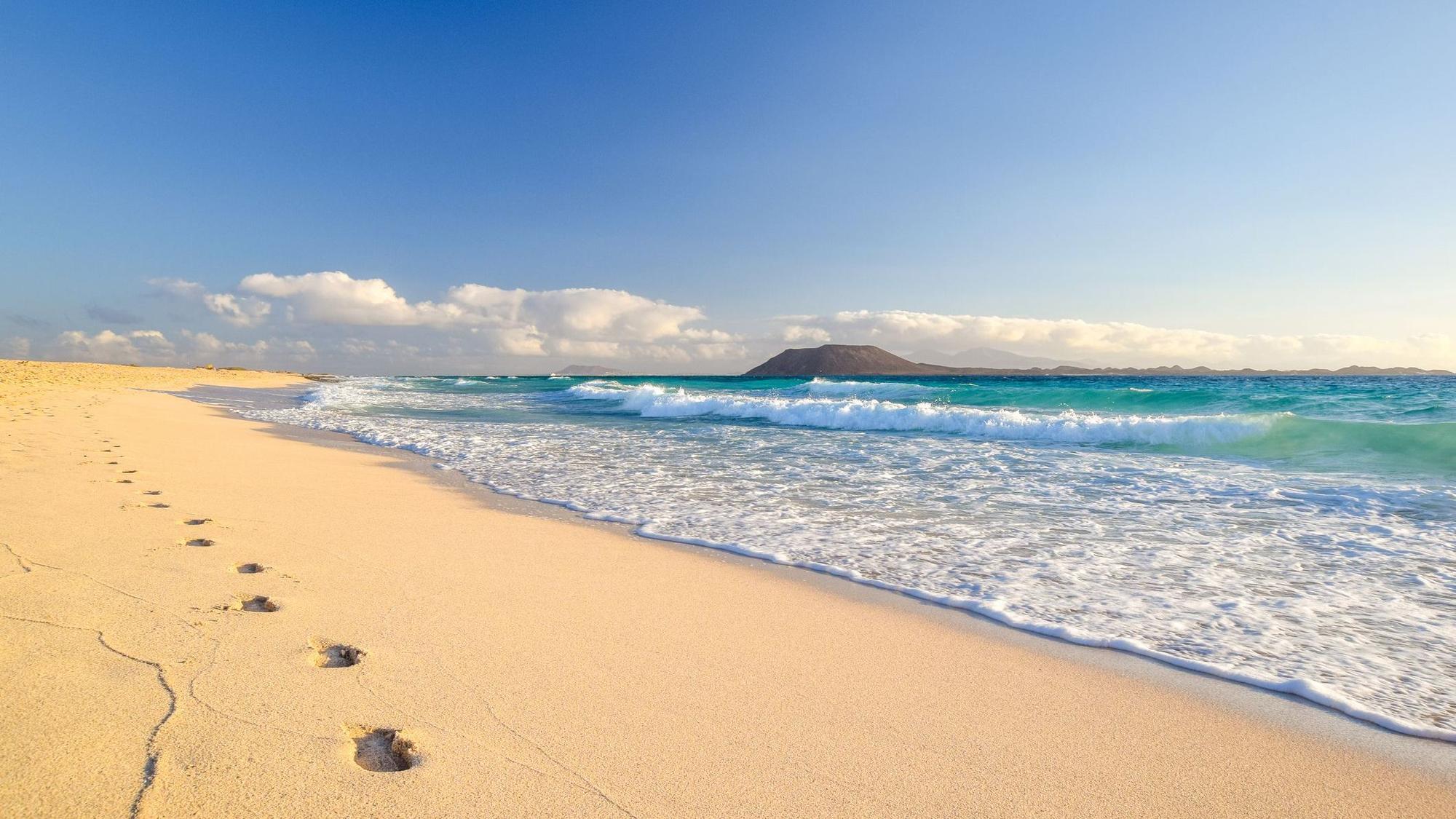 Im Sand sind Fußspuren und am Horizont ist eine Insel zu sehen.