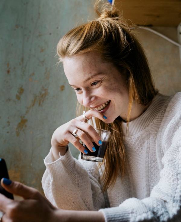 Junge Frau schaut auf ihr Smartphone und lächelt dabei.
