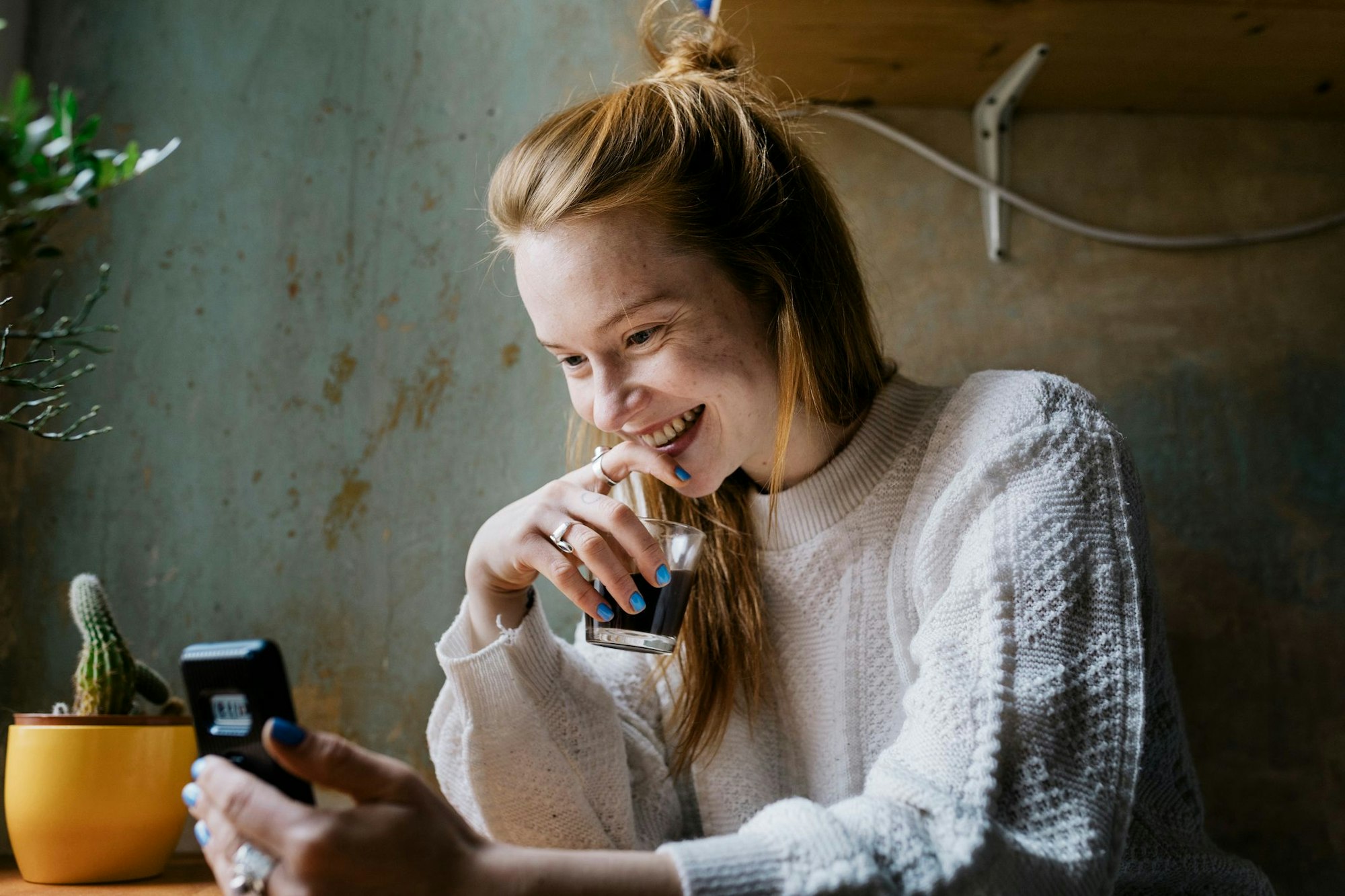 Junge Frau schaut auf ihr Smartphone und lächelt dabei.