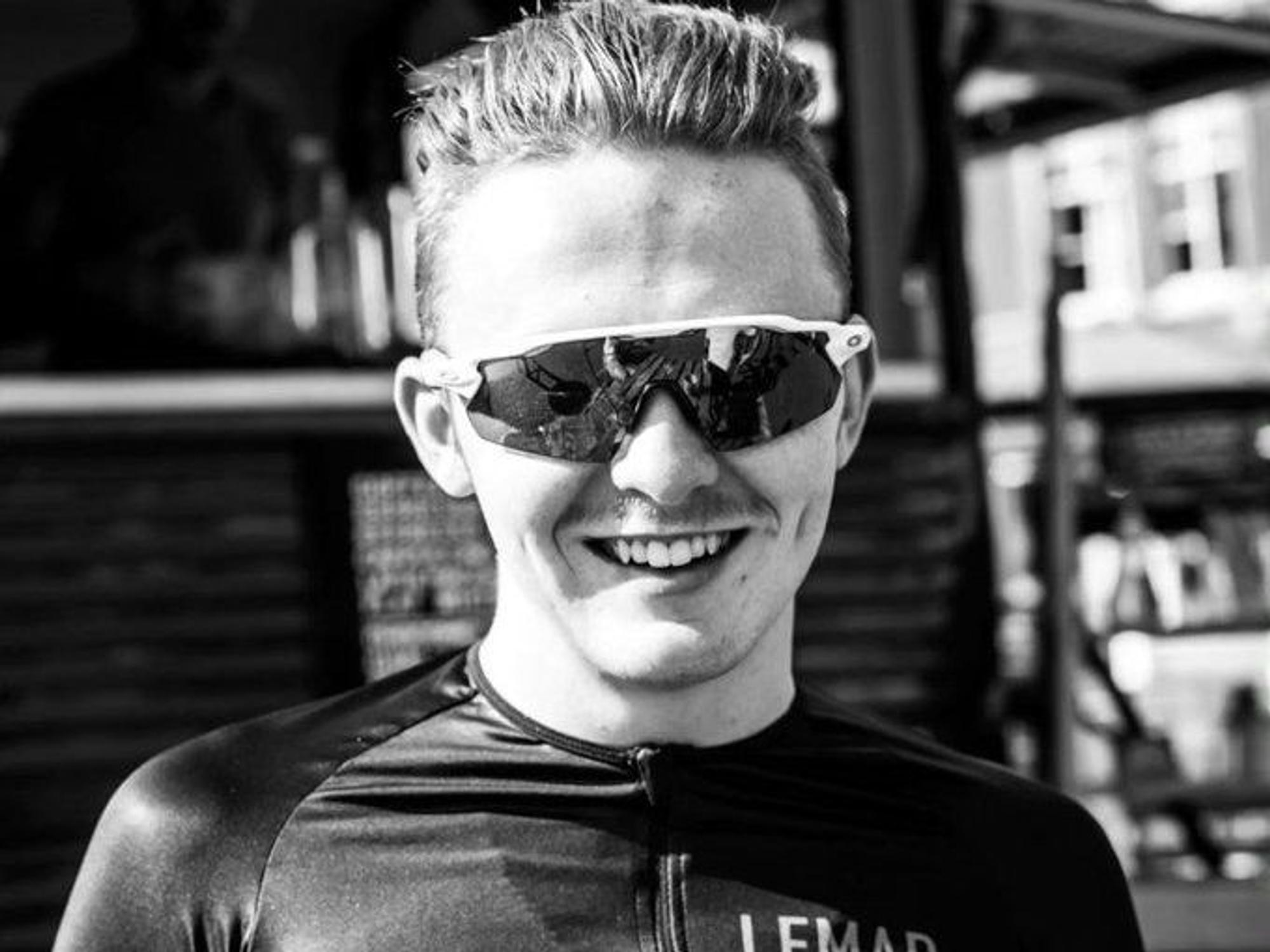Connor Lambert lacht auf einem Schwarz-Weiß-Bild mit Sonnenbrille in die Kamera.