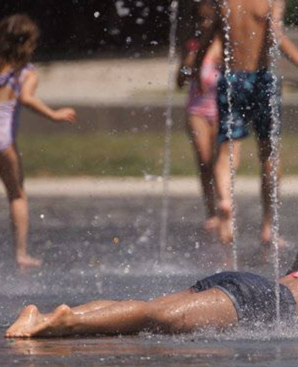Kinder kühlen sich in einem Brunnen ab. Zu viel Hitze tut dem Körper nicht gut. Im Sommer sollten wir uns daher gut schützen.