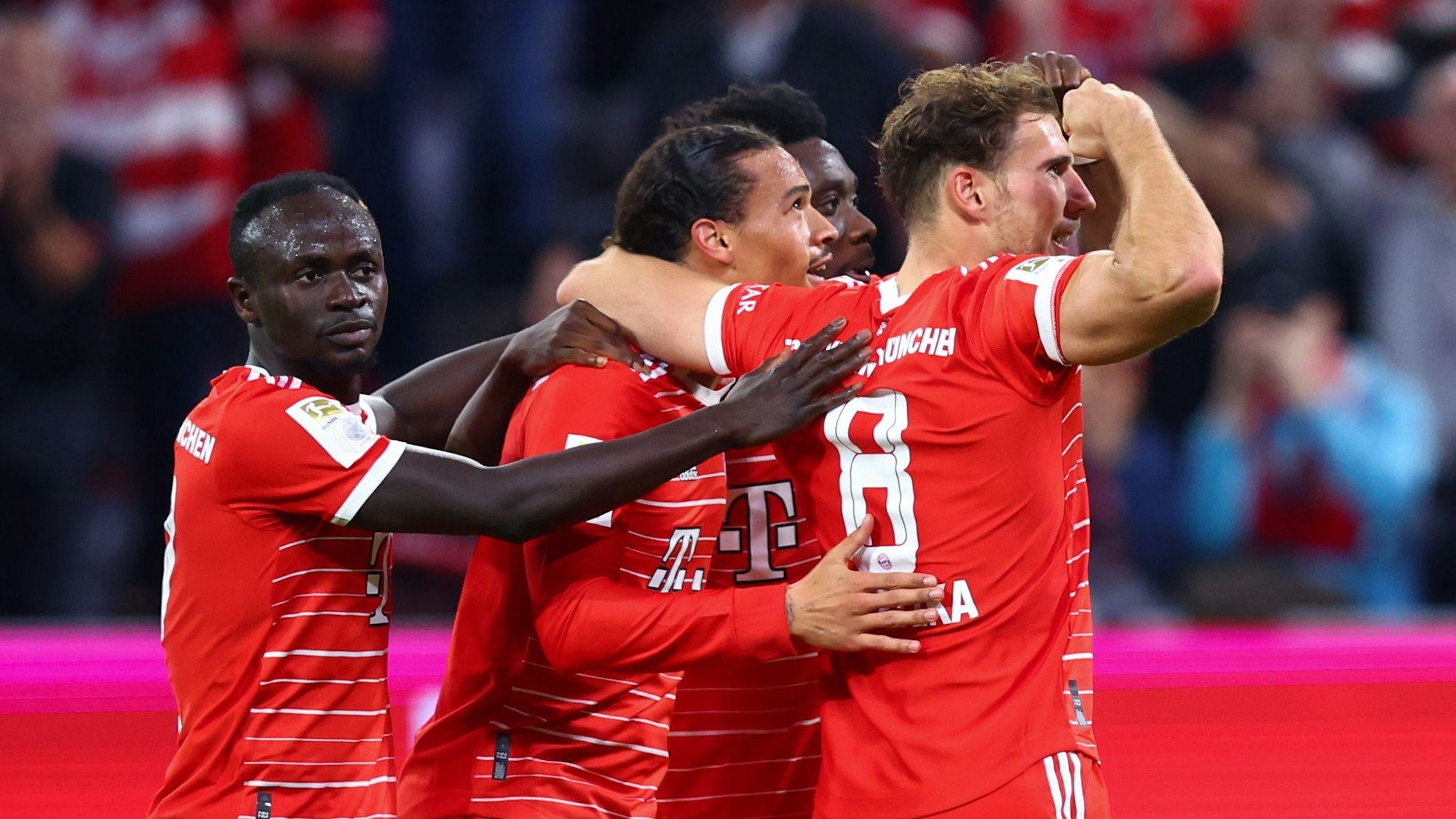 Die Bayern-Spieler Sadio Mané, Leroy Sané und Leon Goretzka feiern ein Tor gegen den SC Freiburg. Sie umarmen Sané, der in der Mitte steht.