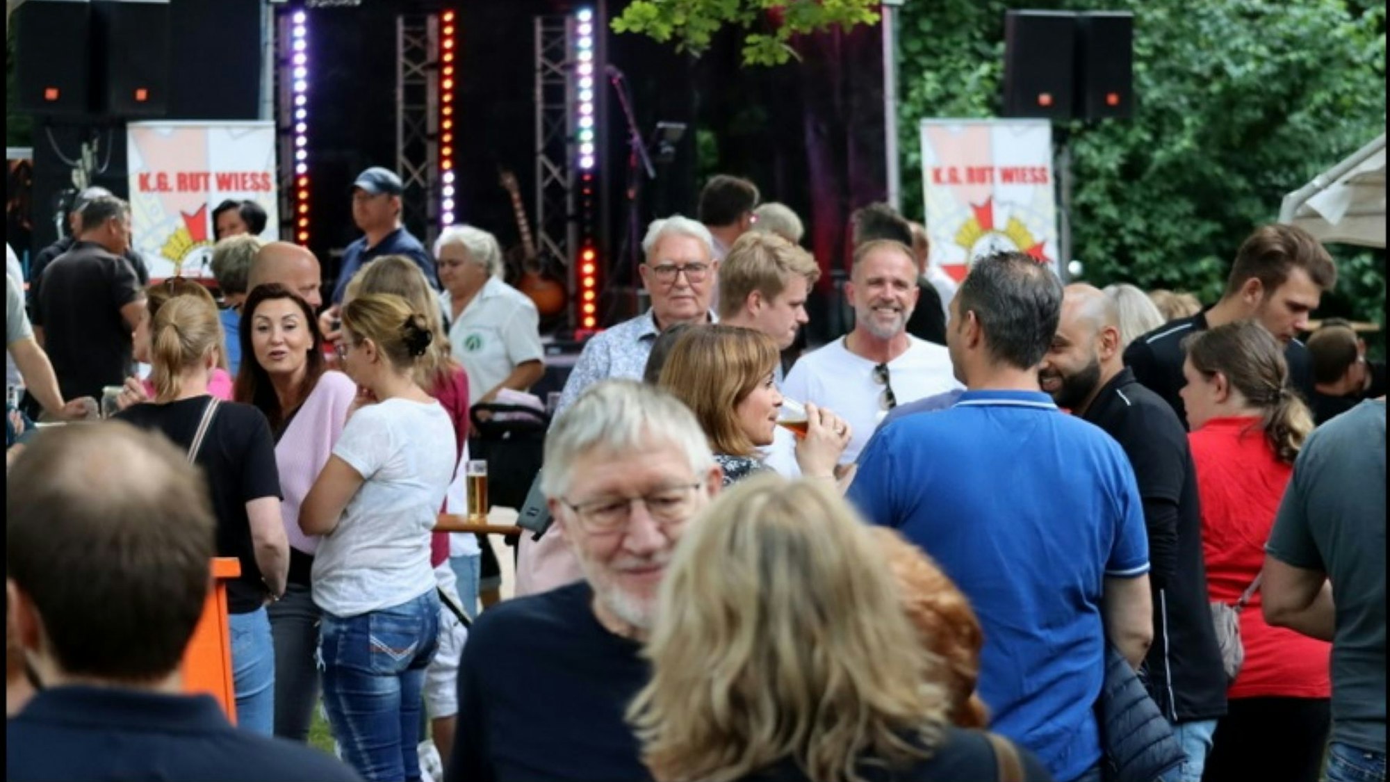 Menschen stehen vor einer Bühne, unterhalten sich.