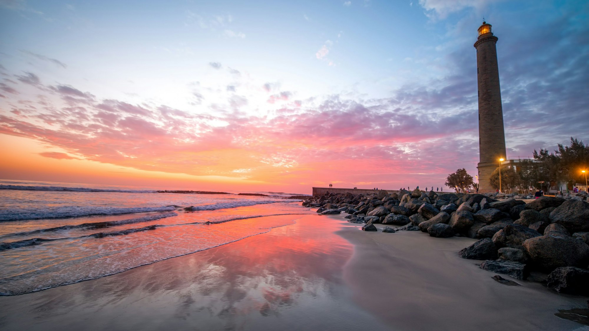 Auf dem Foto sieht man die Playa de Maspalomas samt Leuchtturm im Sonnenuntergang.
