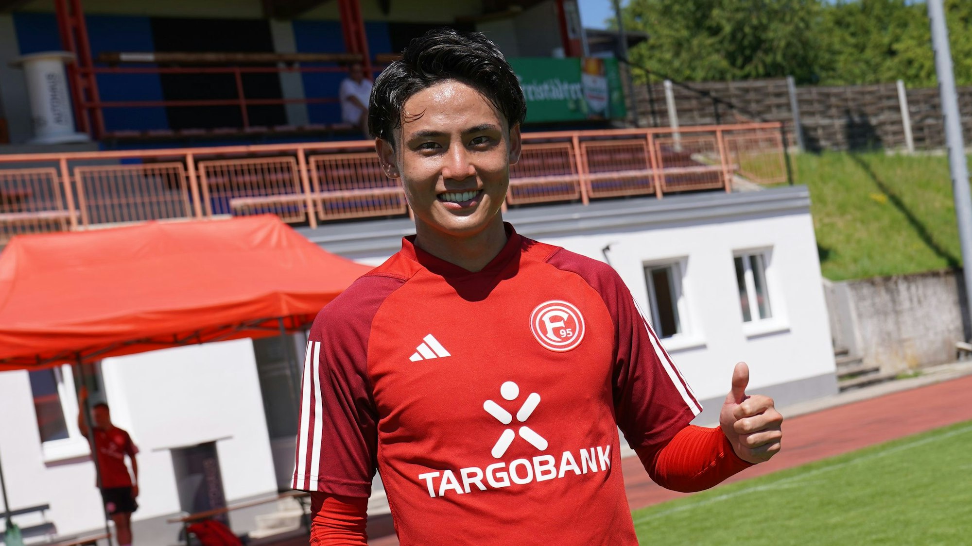 Takashi Uchino posiert auf dem Trainingsplatz für die Kamera und hebt den Daumen.