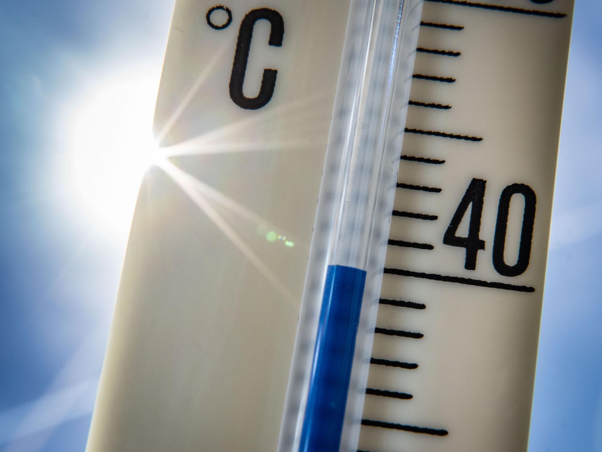 Ein Außenthermometer zeigt vor dem blauen Himmel und der Sonne eine Temperatur von nahezu 40 Grad Celsius an, hier im Juli 2022 in Frankfurt am Main.