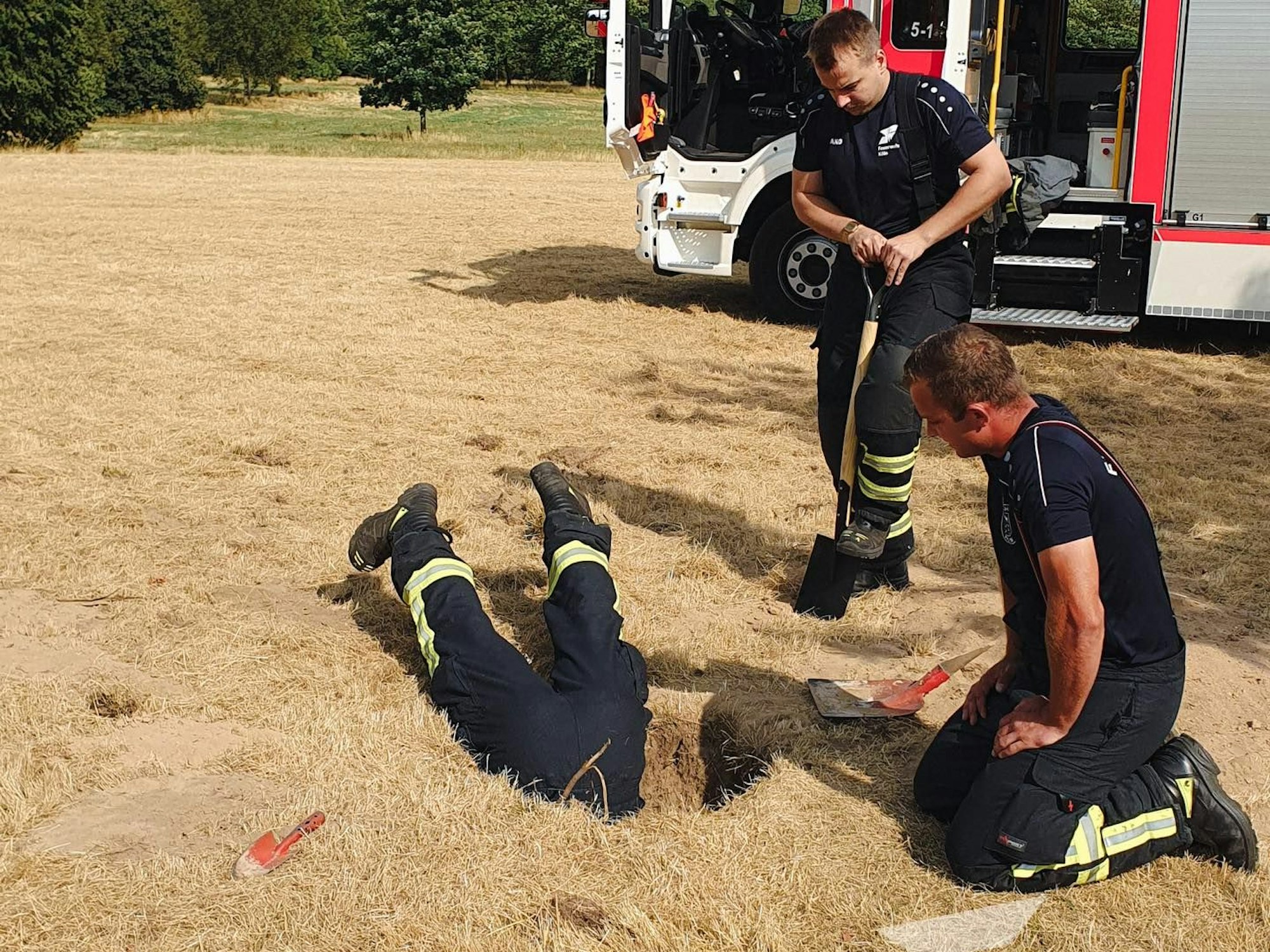 Ein Feuerwehrmann hängt kopfüber im Kaninchenbau, zwei Kollegen gucken zu.