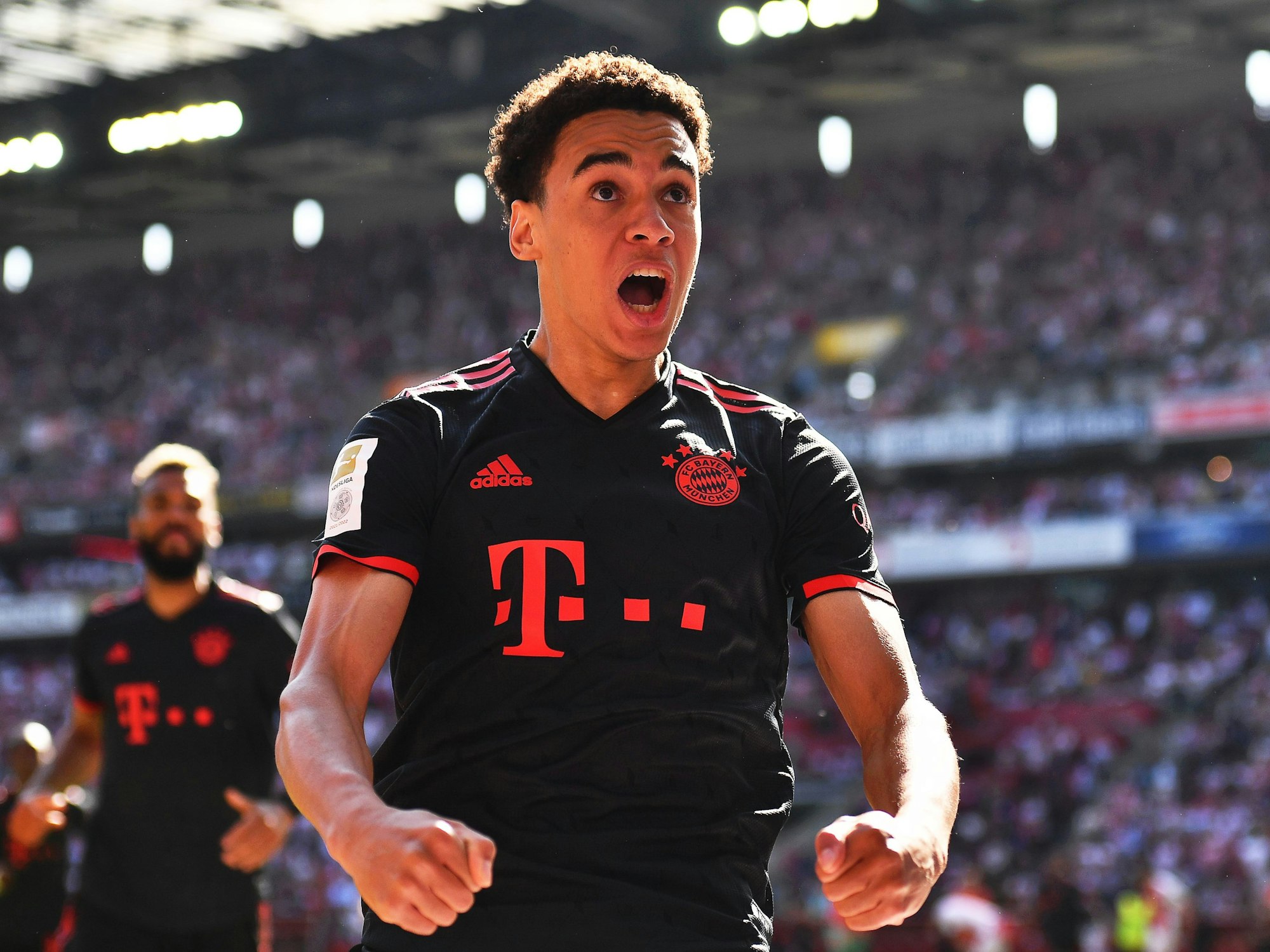 Jamal Musiala, im schwarzen Bayern-Trikot, reißt den Mund auf und ballt beide Fäuste vor seinem Körper.