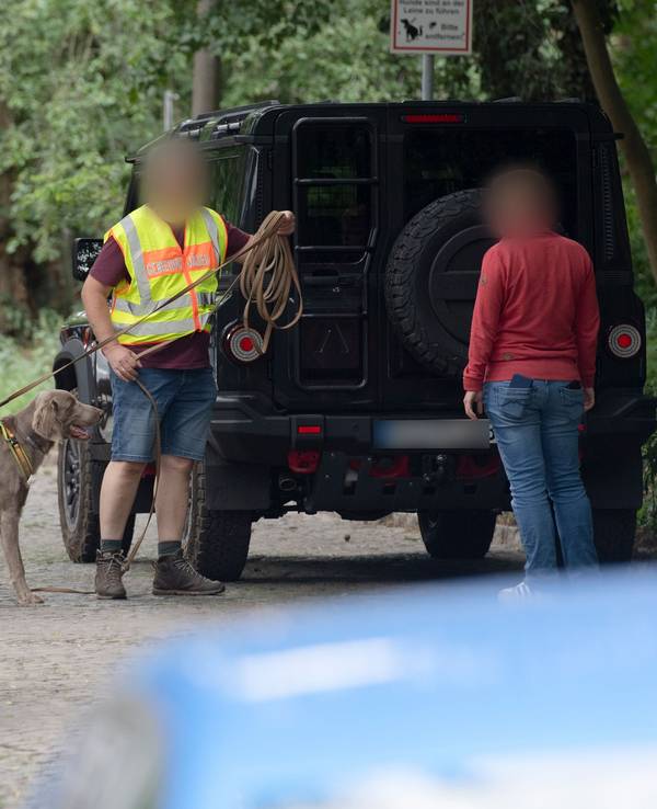 Zwei Männer, davon einer mit Hund und einer Weste mit Aufschrift, stehen an einem Fahrzeug.