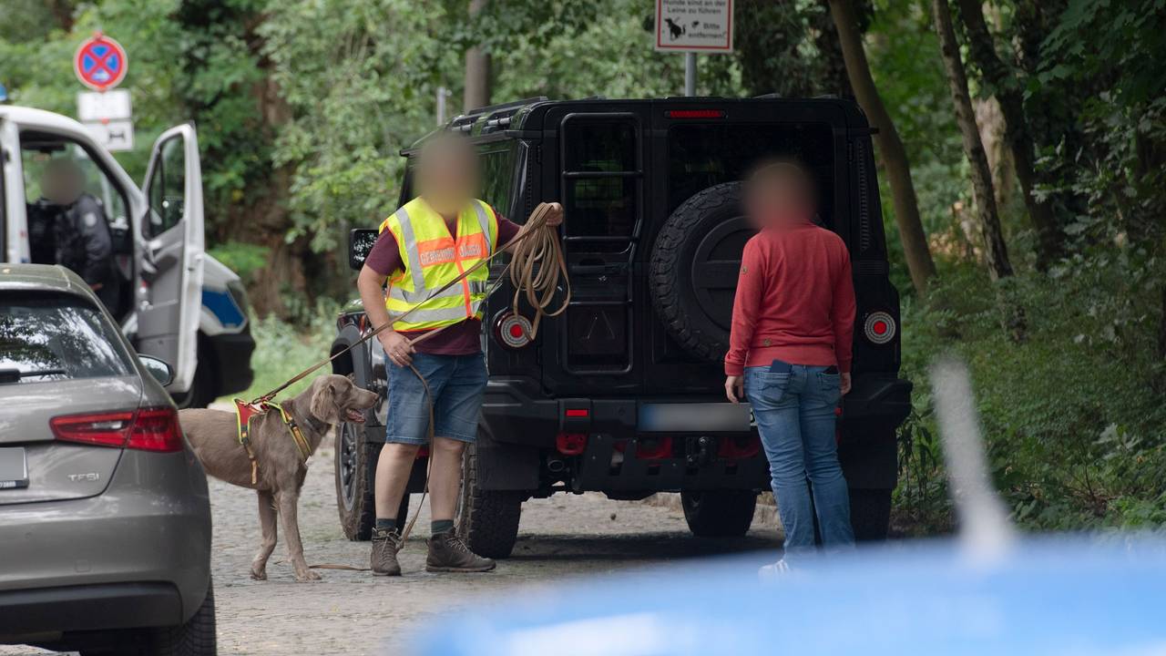 Zwei Männer, davon einer mit Hund und einer Weste mit Aufschrift, stehen an einem Fahrzeug.