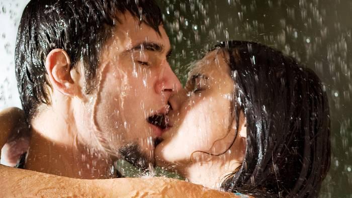 Young happy amorous couple hugging and kissing under a rain, outdoors