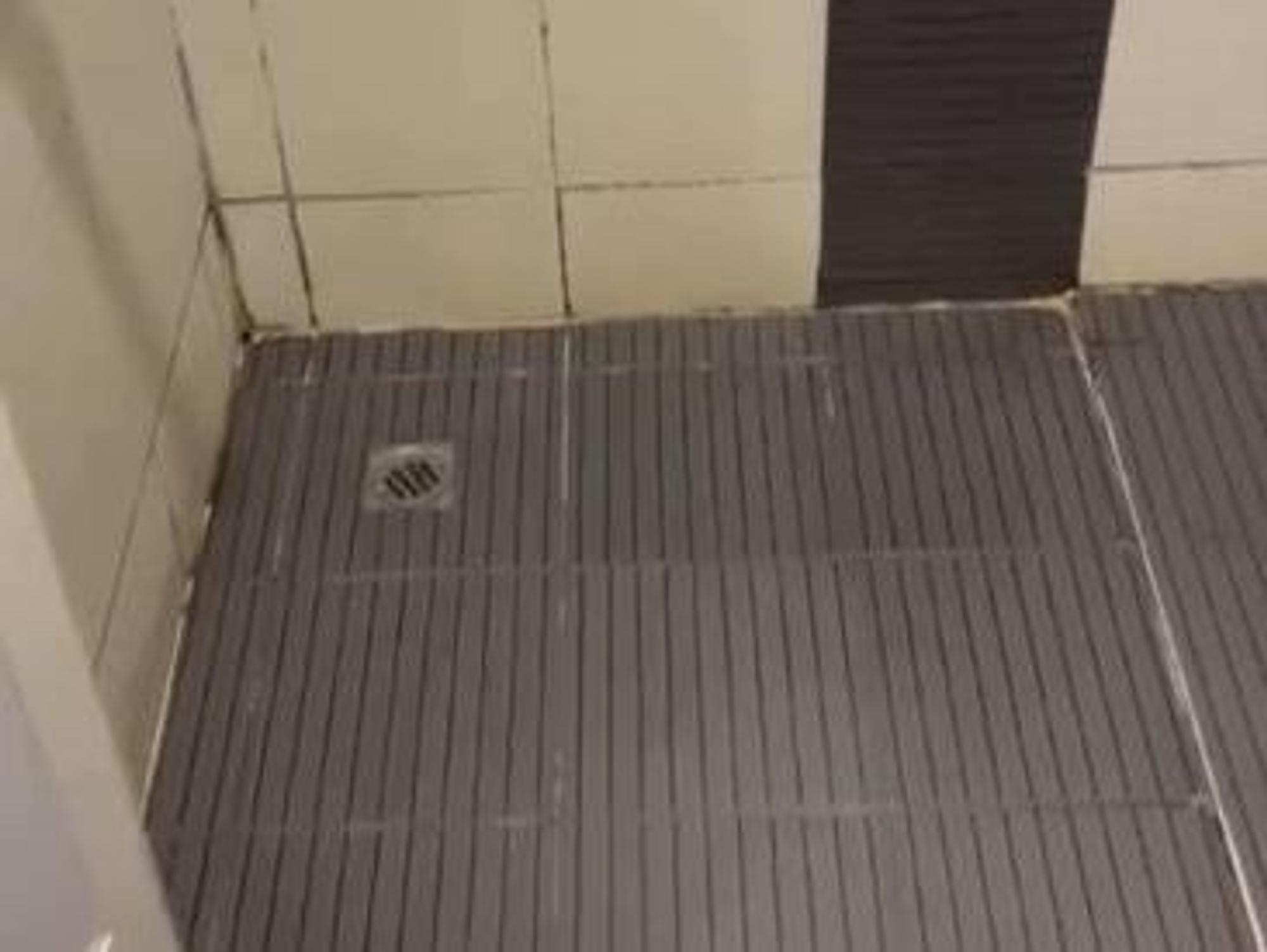 Blick in die Dusche eines Hotels. Dort sind Schimmel und ein verdreckter Abfluss zu sehen.