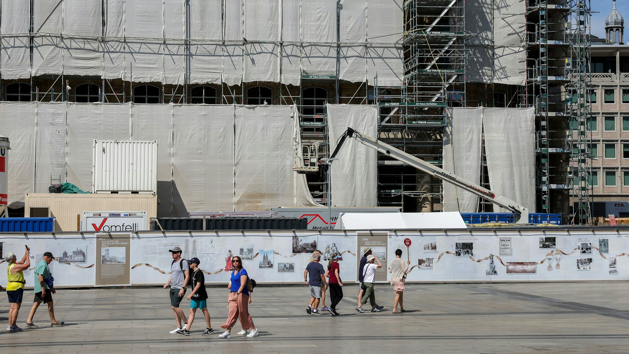 Menschen laufen an einer Baustelle rundum den Kölner Dom vorbei.