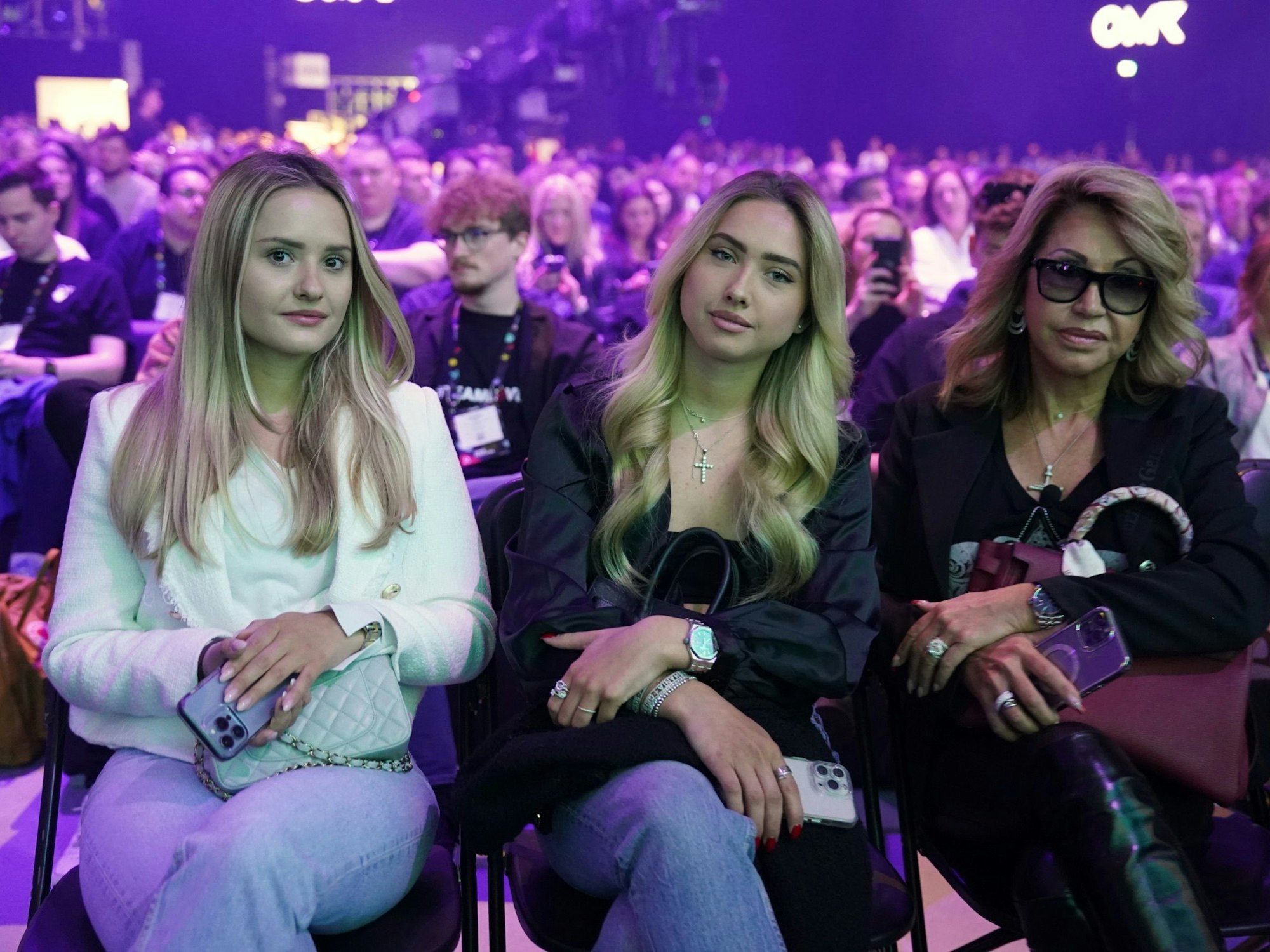 Davina (l-r) und Shania Geiss sitzen neben ihrer Mutter Carmen Geiss während des Auftritts von Robert Geiss, Unternehmer und TV-Reality-Star, auf der Bühne der Digital-Messe OMR in den Messehallen.