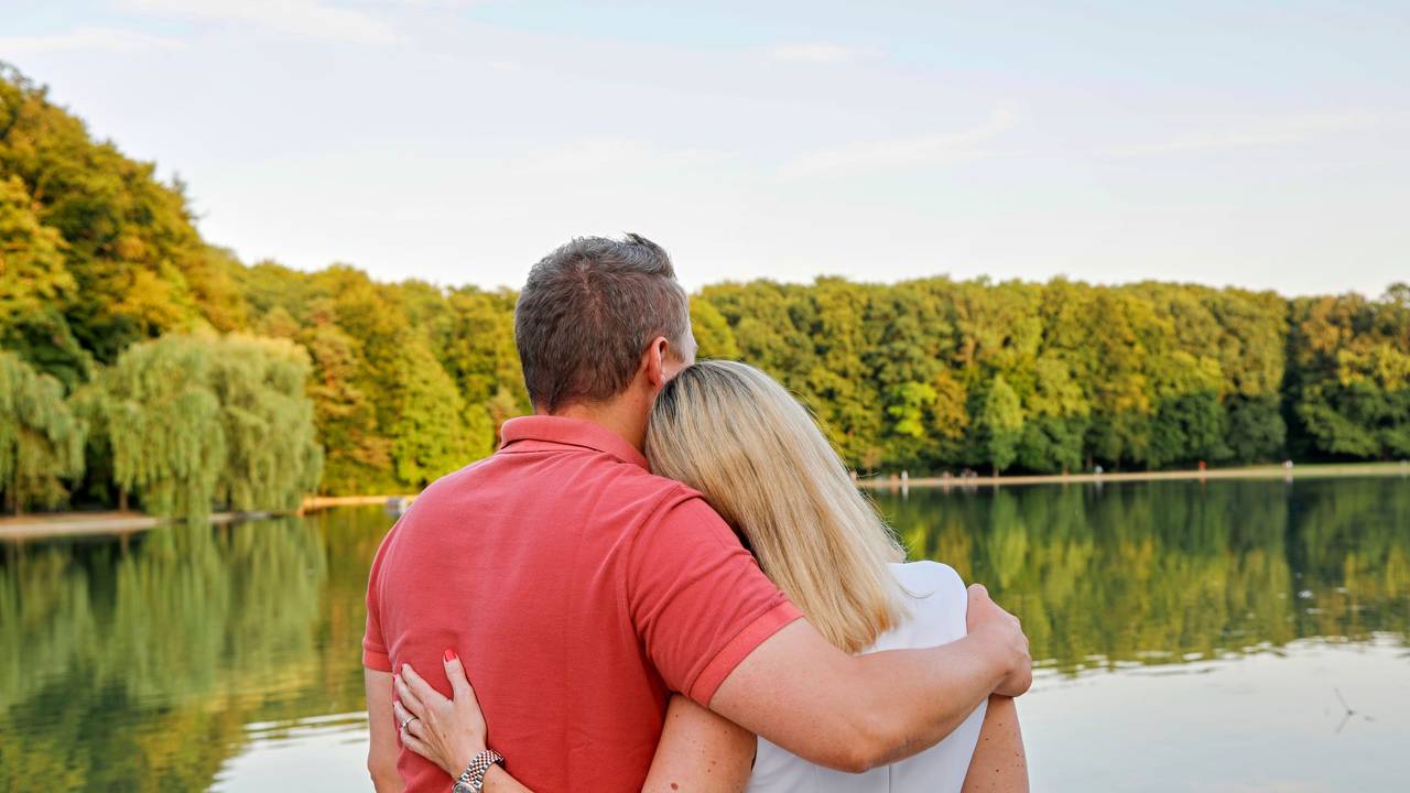 Tanja Wolters und Michael Gerhold stehen mit dem Rücken zur Kamera am Adenauerweiher in Köln und blicken in die Ferne.