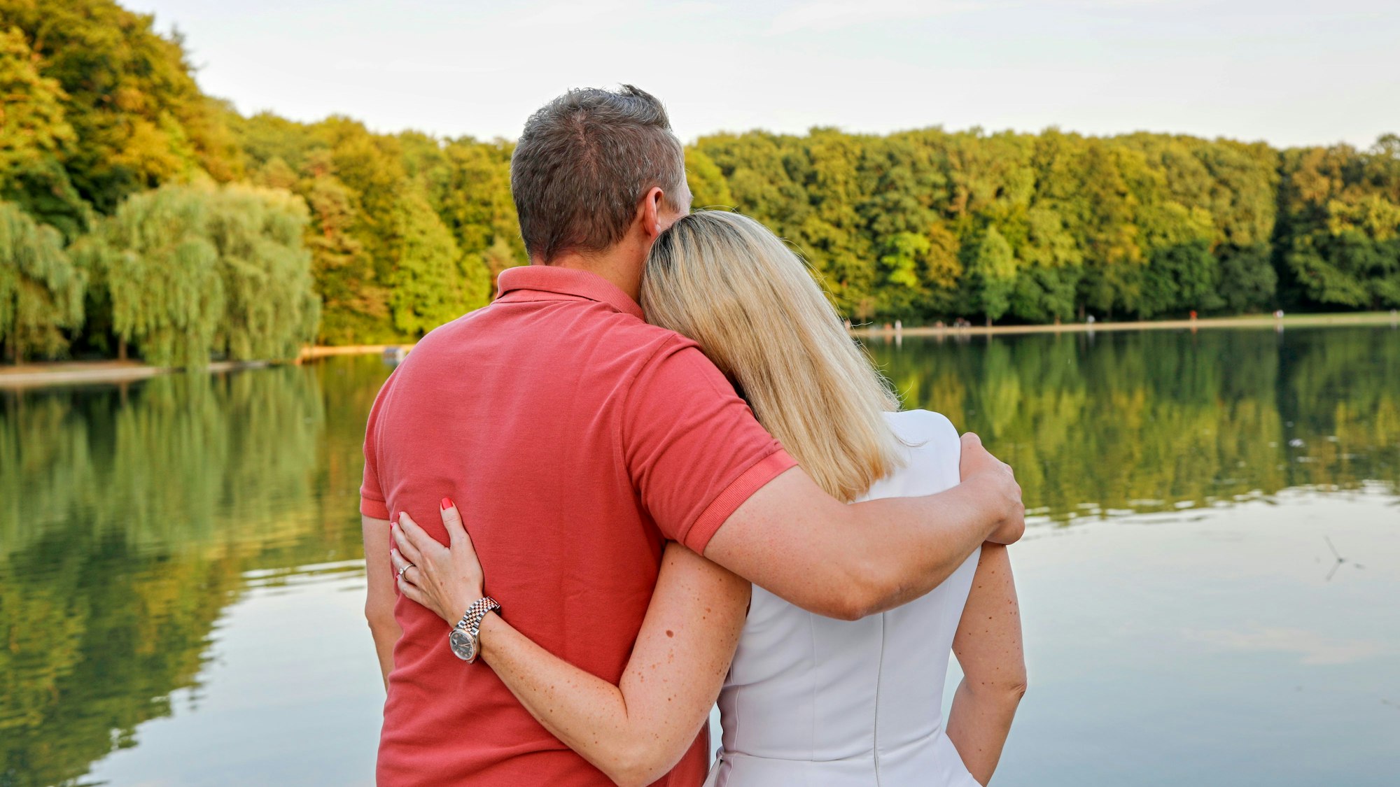 Tanja Wolters und Michael Gerhold stehen mit dem Rücken zur Kamera am Adenauerweiher in Köln und blicken in die Ferne.