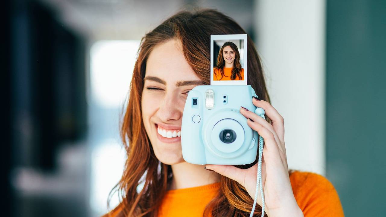 Frau hält Sofortbild-Kamera mit Bild in der Hand