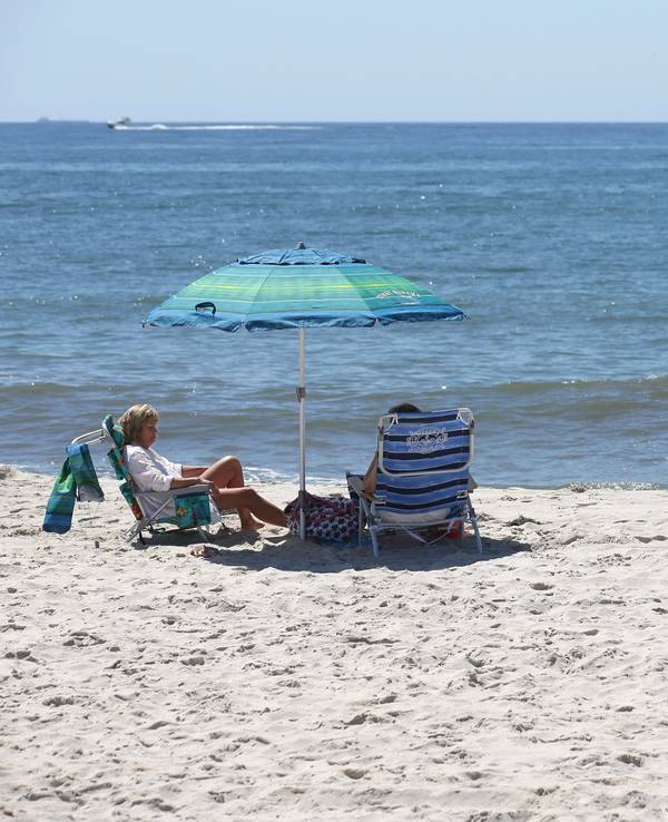 Zwei Menschen sitzen am Strand, neben ihnen steht ein Schild mit der Aufschrift "Vorsicht, nicht schwimmen".