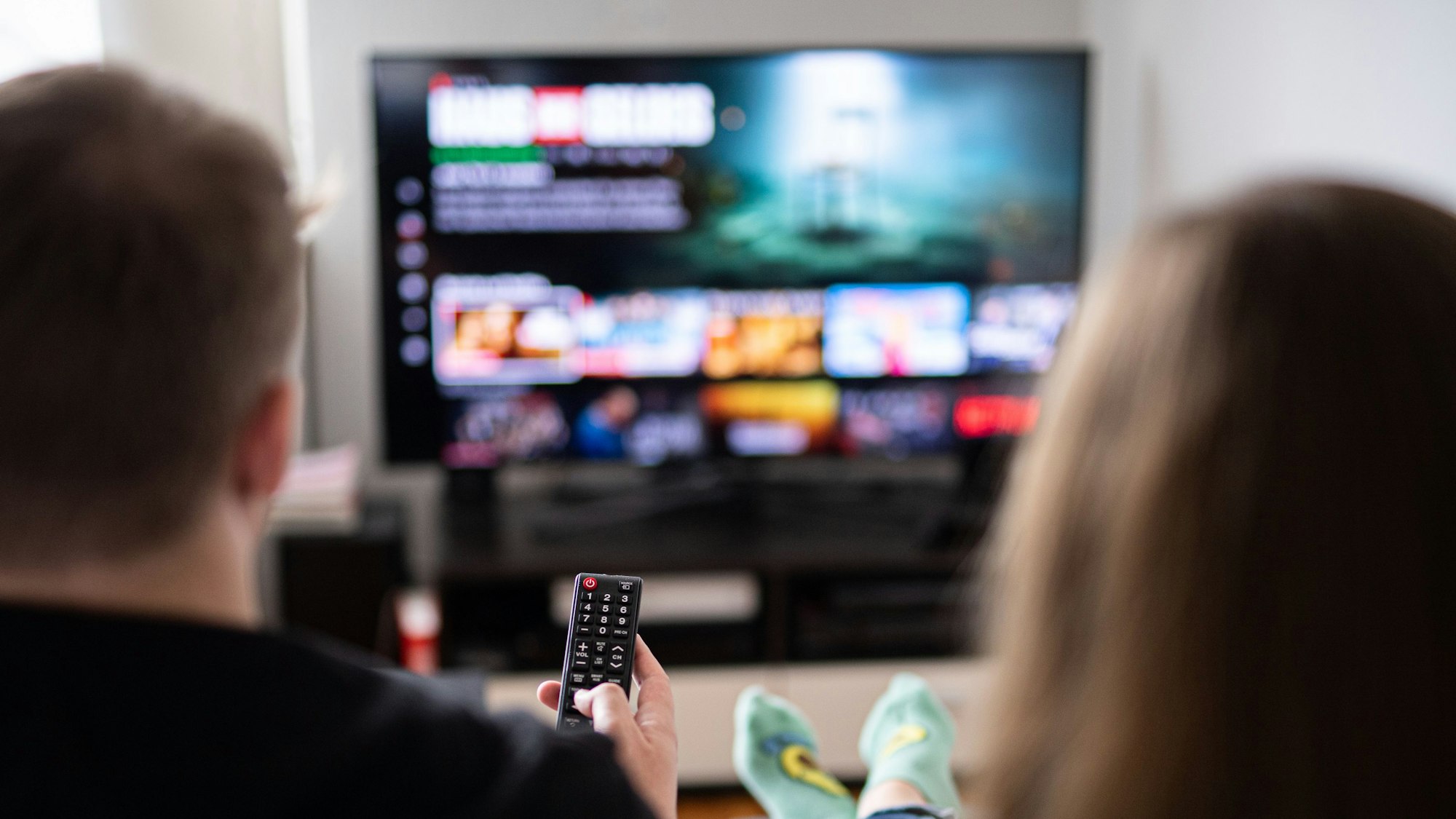 Das Foto zeigt ein Paar, das vor dem Fernseher sitzt.