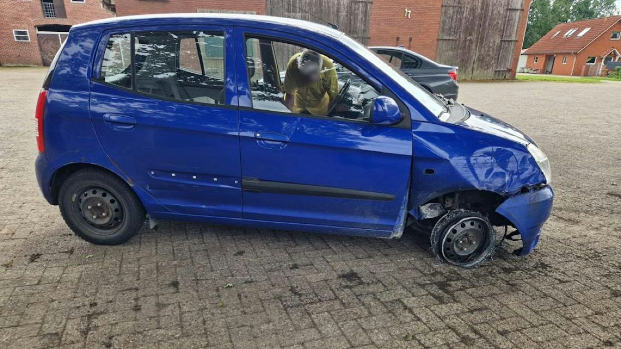 Ein blauer Kia, dem das rechte Vorderrad fehlt.