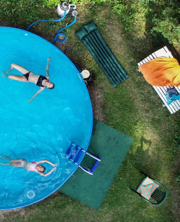 Drei Kinder in einem Swimmingpool, der in einem Garten steht.
