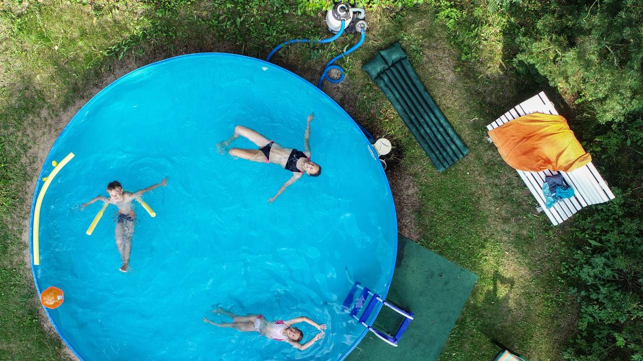 Drei Kinder in einem Swimmingpool, der in einem Garten steht.