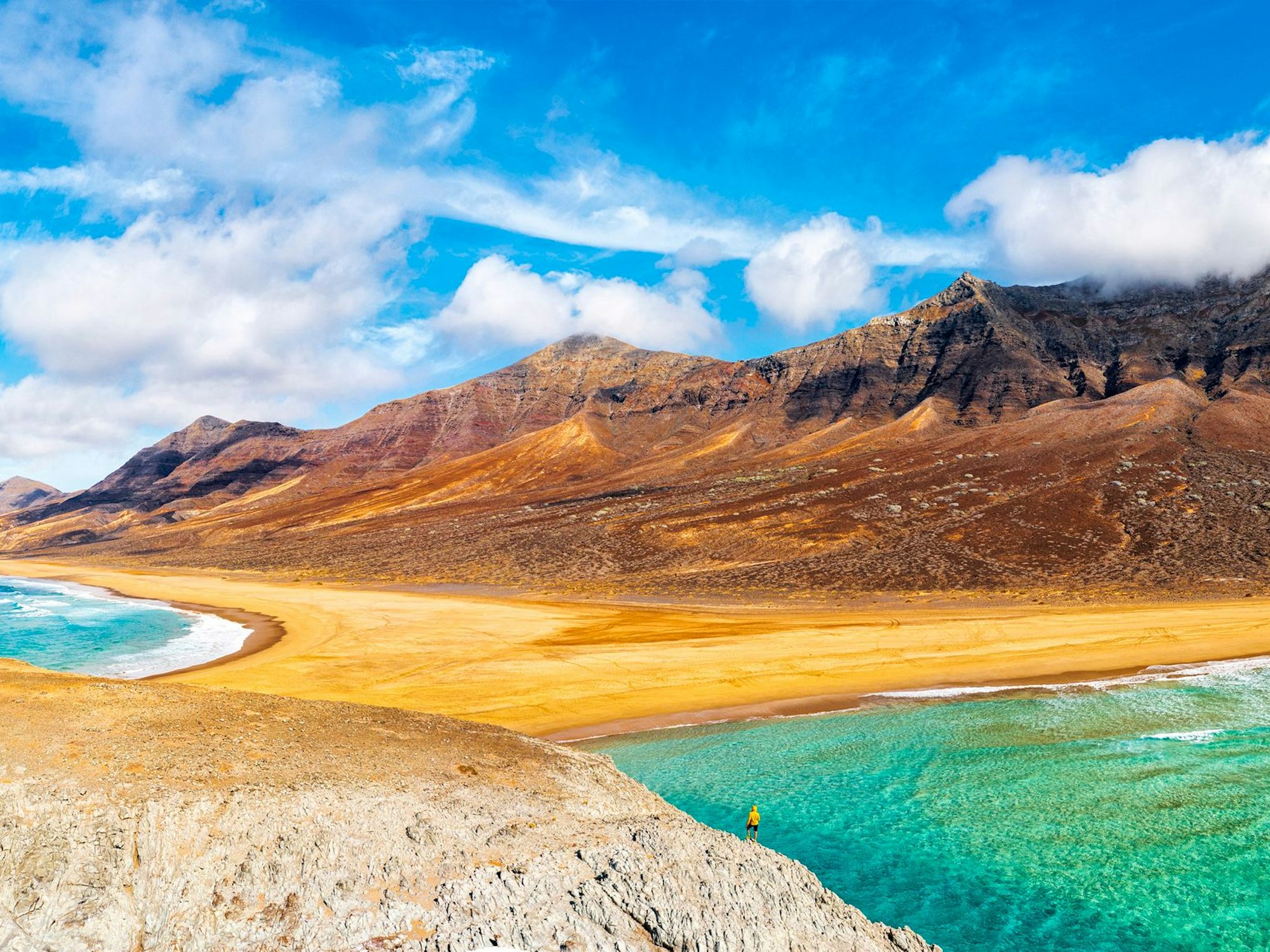 Goldener Sand trifft auf türkisfarbenes Wasser vor braunem Fels.