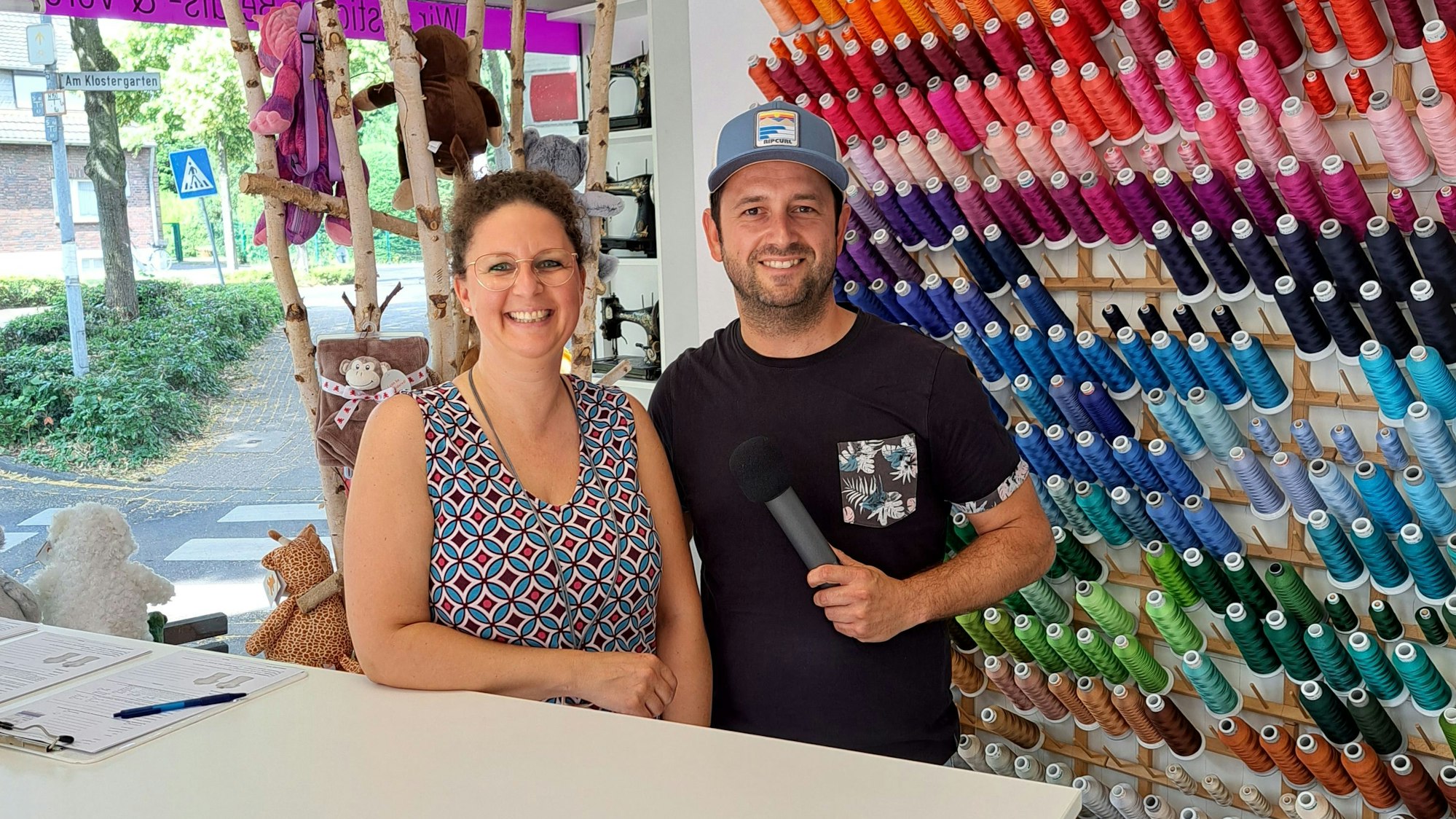 Dominik Becker steht neben Rebecca Wolf in ihrem Laden, die beiden grinsen in die Kamera.