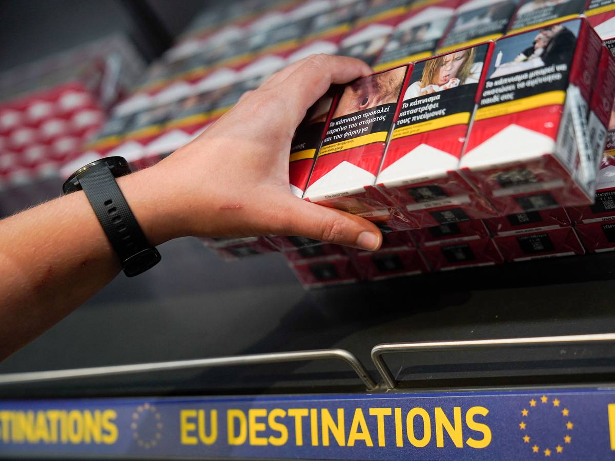 Eine Frau greift in einem Flughafen von einem Regal nach den Zigarettenstangen.