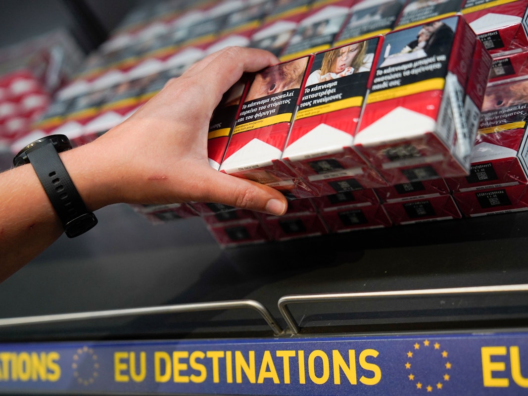 Eine Frau greift in einem Flughafen von einem Regal nach den Zigarettenstangen.