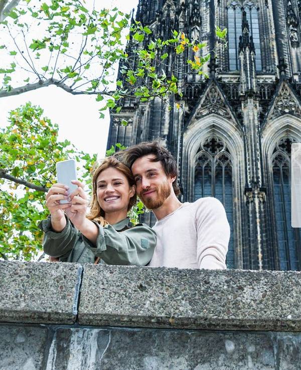 Mann und Frau schießen Selfie vorm Kölner Dom. Daneben das Logo der Website Bütz mich.