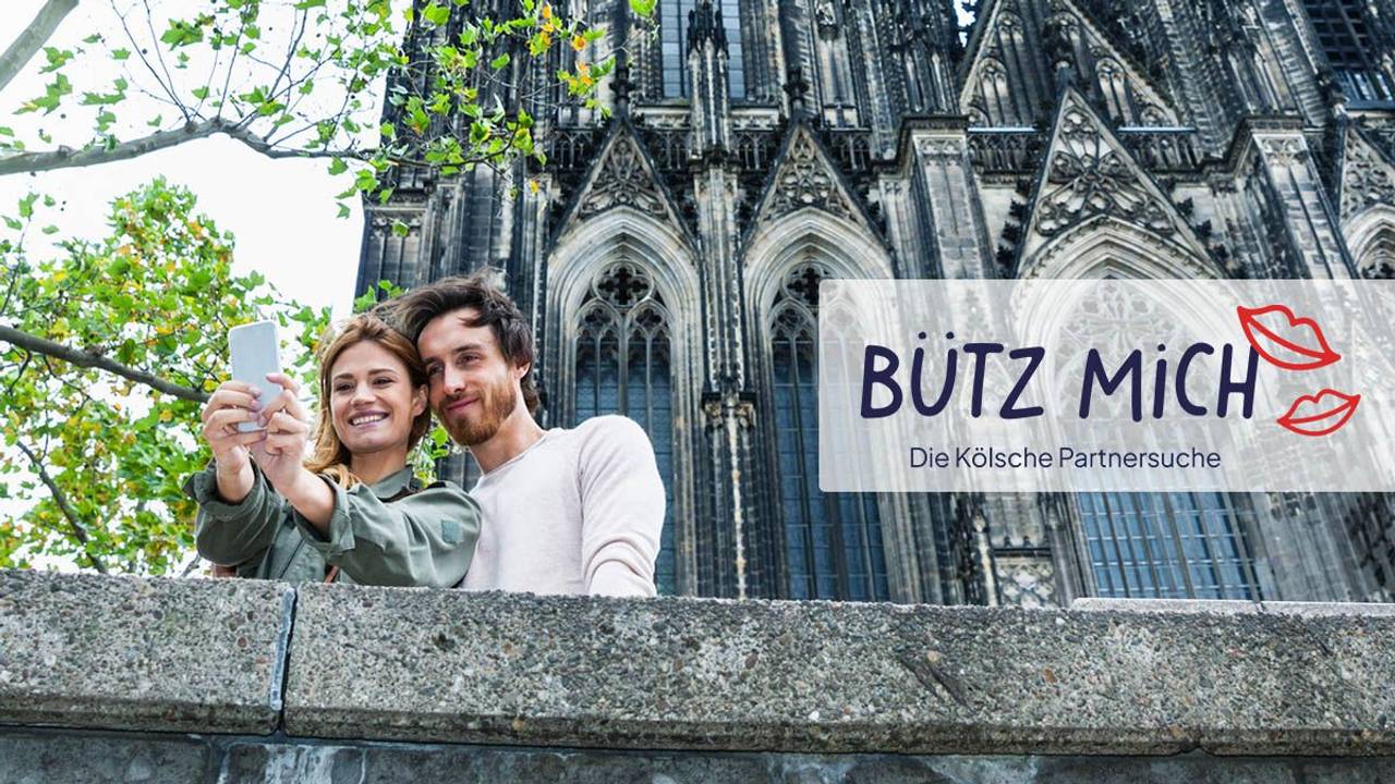 Mann und Frau schießen Selfie vorm Kölner Dom. Daneben das Logo der Website Bütz mich.