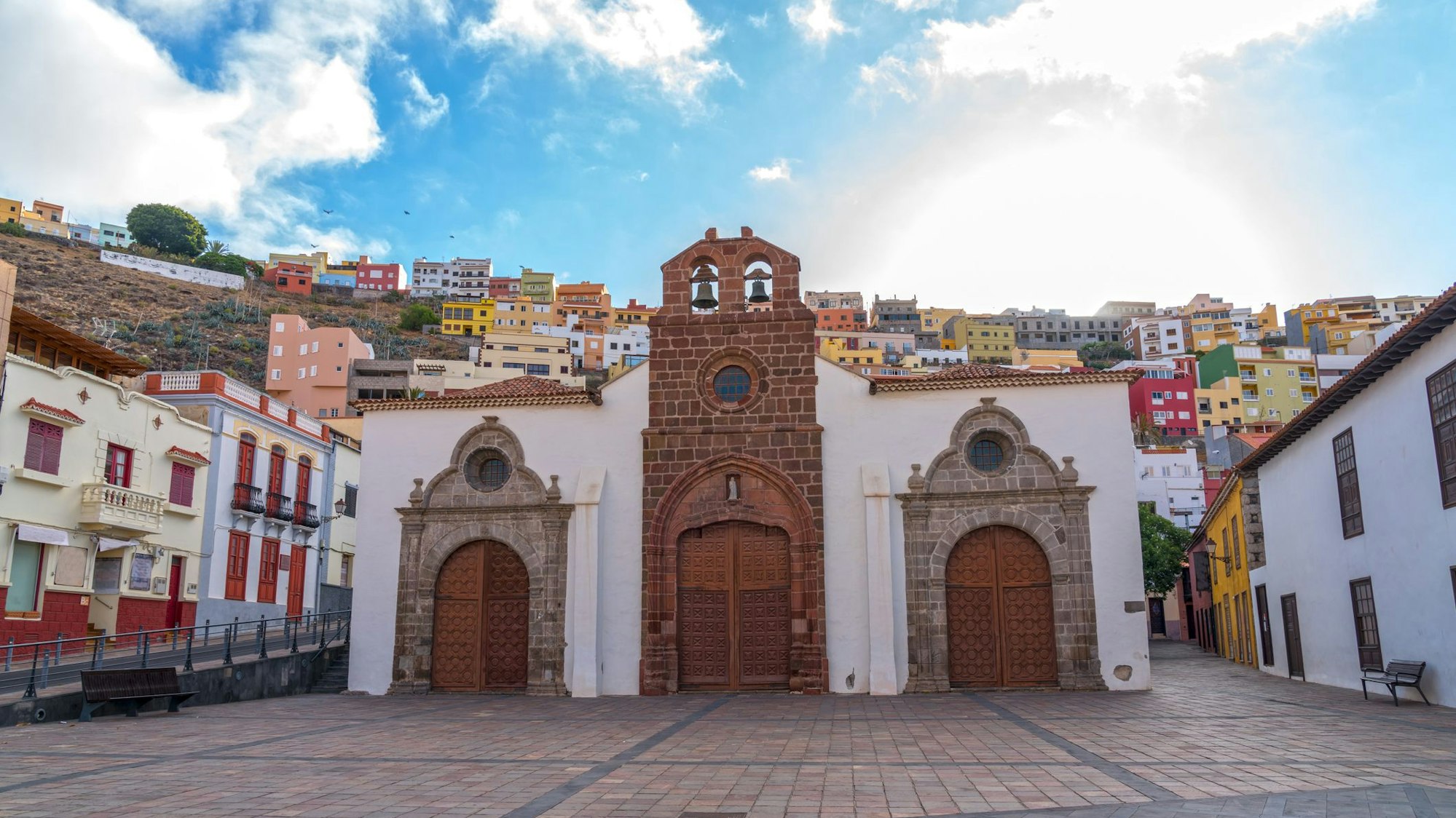 Eine kleine, steinerne Kirche steht vor farbenfrohen Häusern.