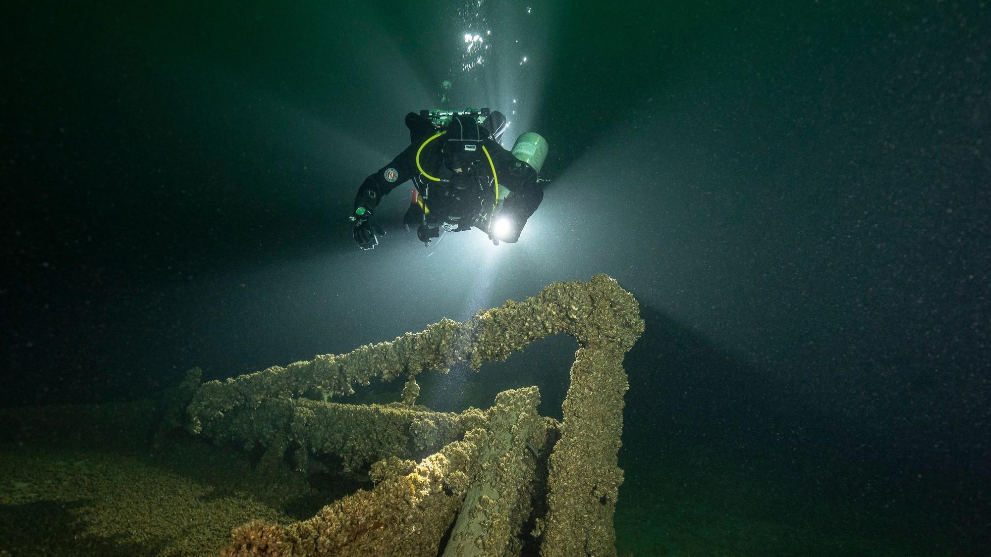 Ein Taucher beleuchtet ein Schiffswrack im Bodensee mit einer Lampe.