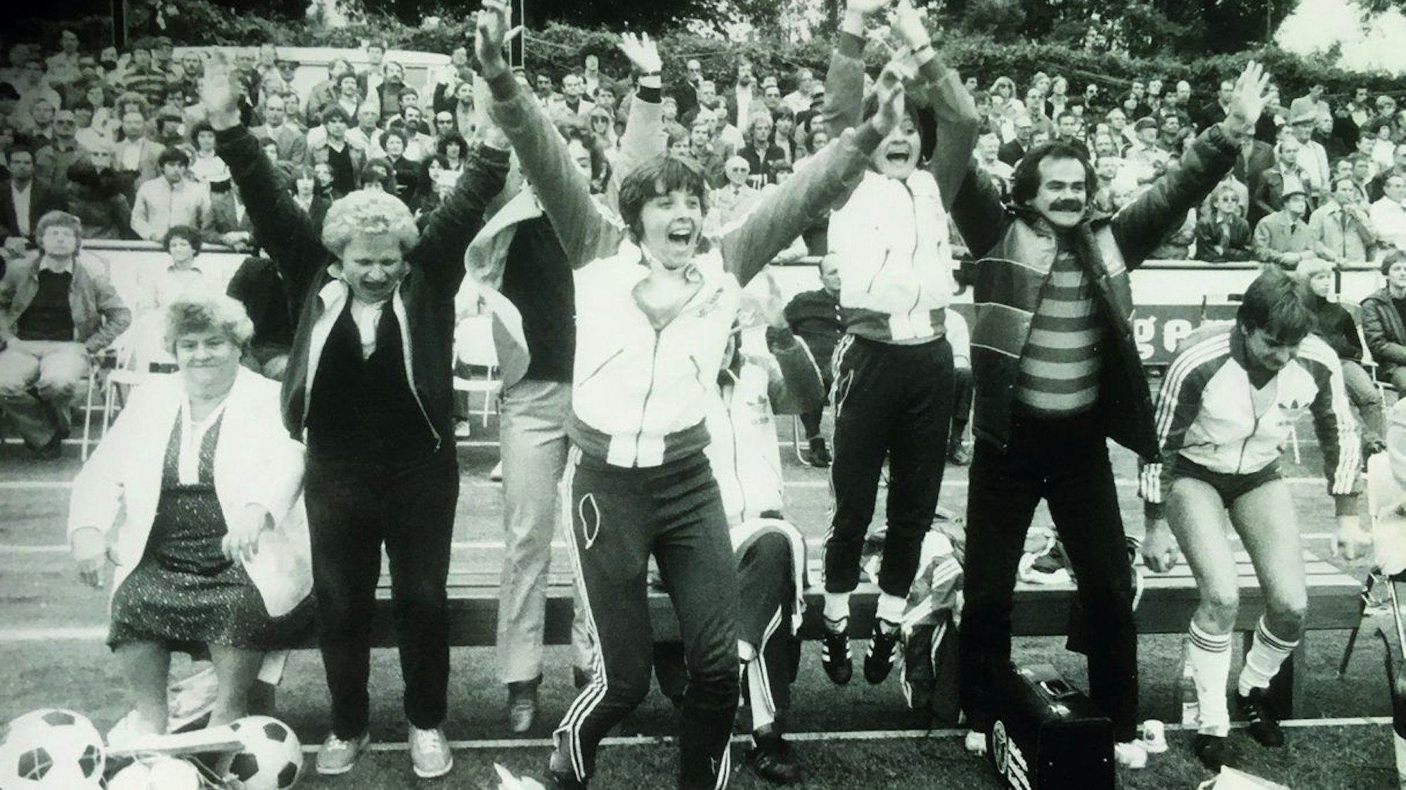 Mehrere Frauen und ein Mann springen jubelnd von der Bank am Spielfeldrand auf.