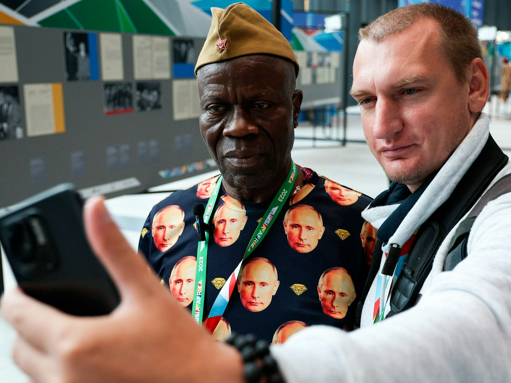 Lama Jacques Sevoba (l.), Botschaftsmitarbeiter aus Guinea, trägt ein T-Shirt mit Fotos des russischen Präsidenten Putin. Er sorgte mit seinem Outfit für Wirbel.