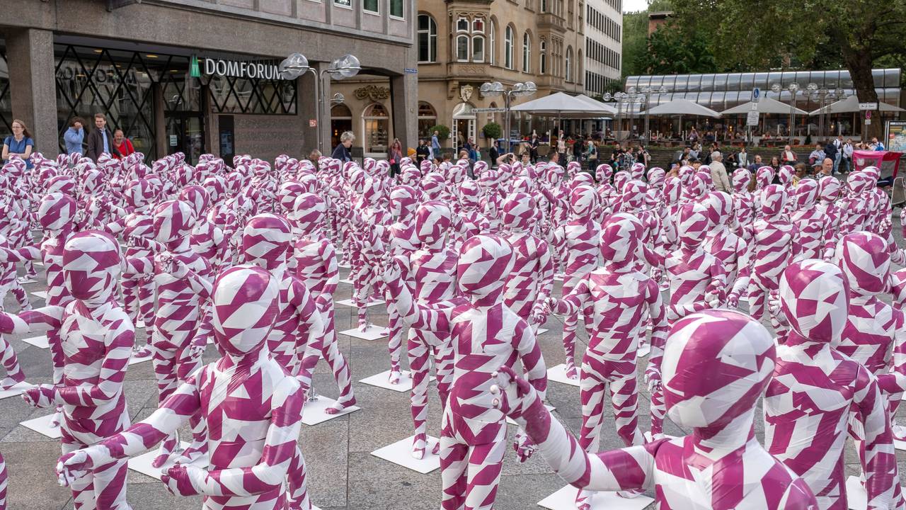 333 Kinderfiguren in purpur-weißem Flatterband vor dem Kölner Dom