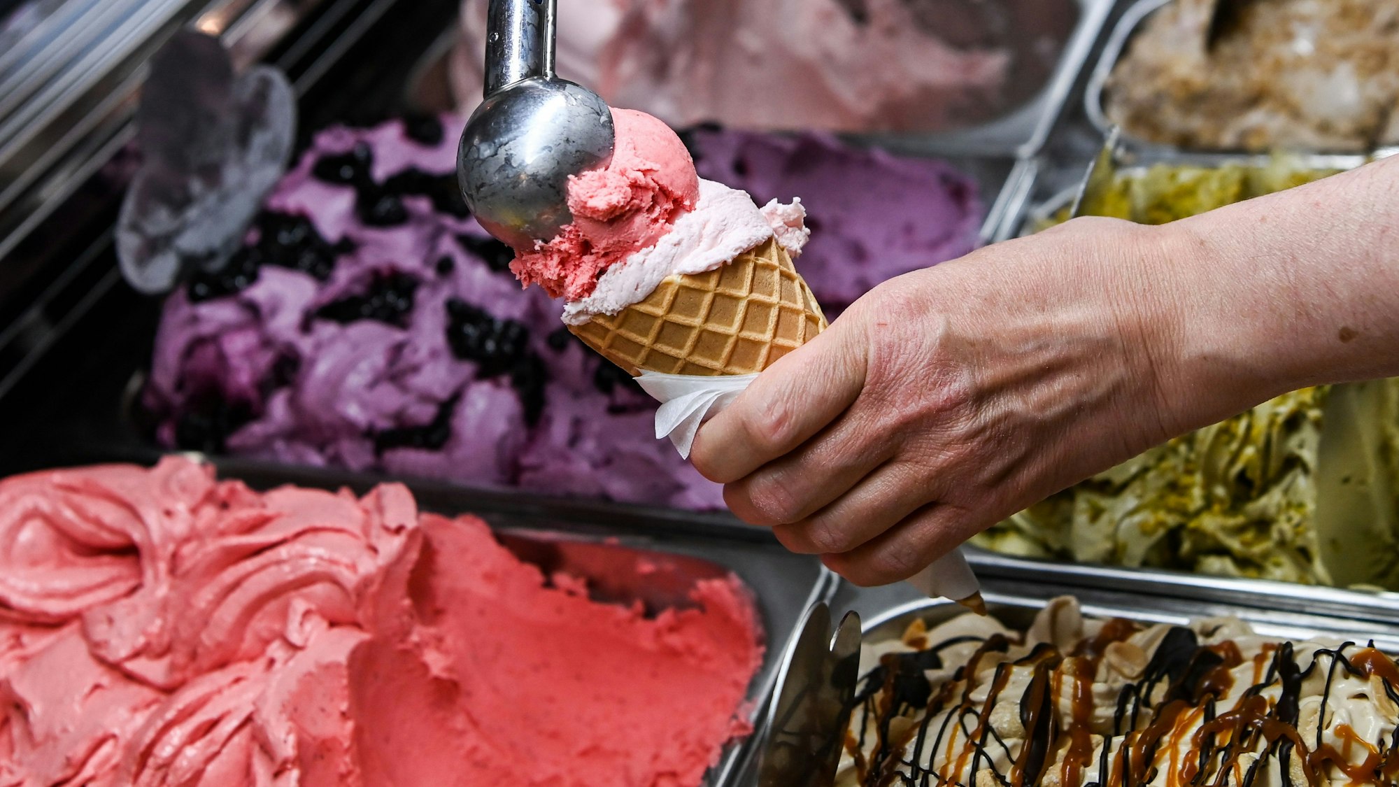 Eine Kugel Erdbeereis wird in der Eisdiele auf eine weitere Kugel in einer Waffel gesetzt.