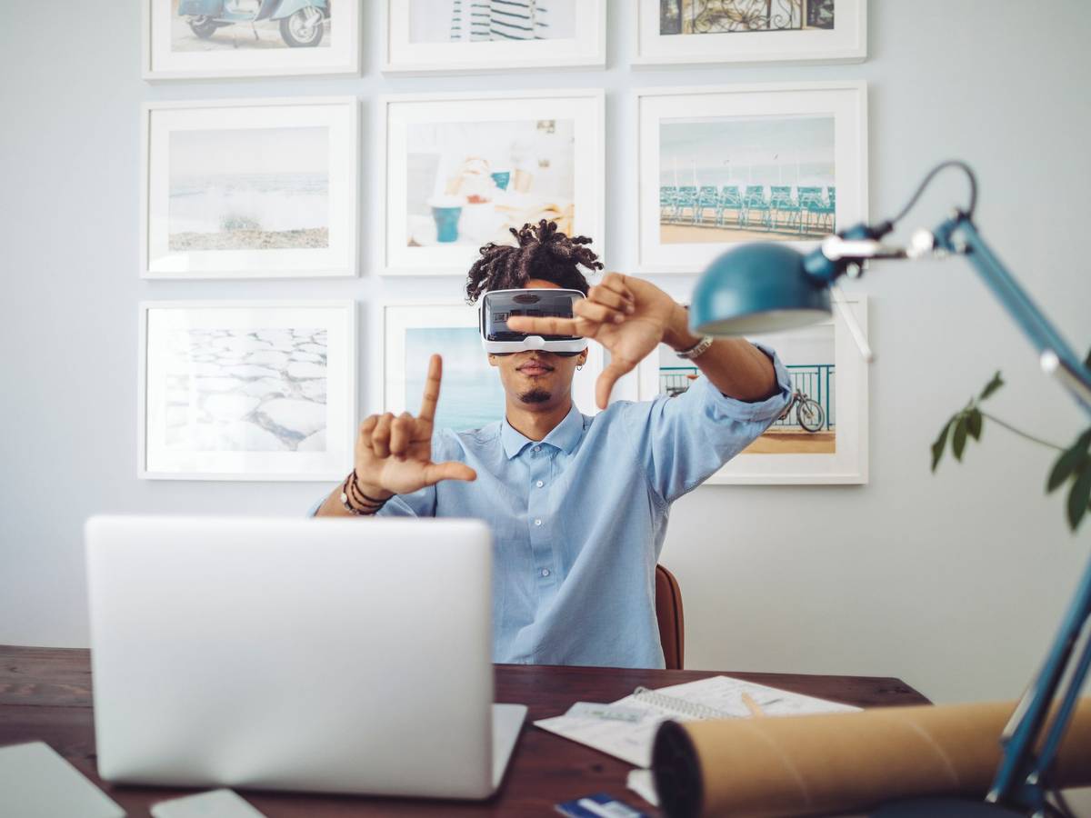 Mann sitzt am Schreibtisch vorm Laptop mit Virtual Reality Brille.