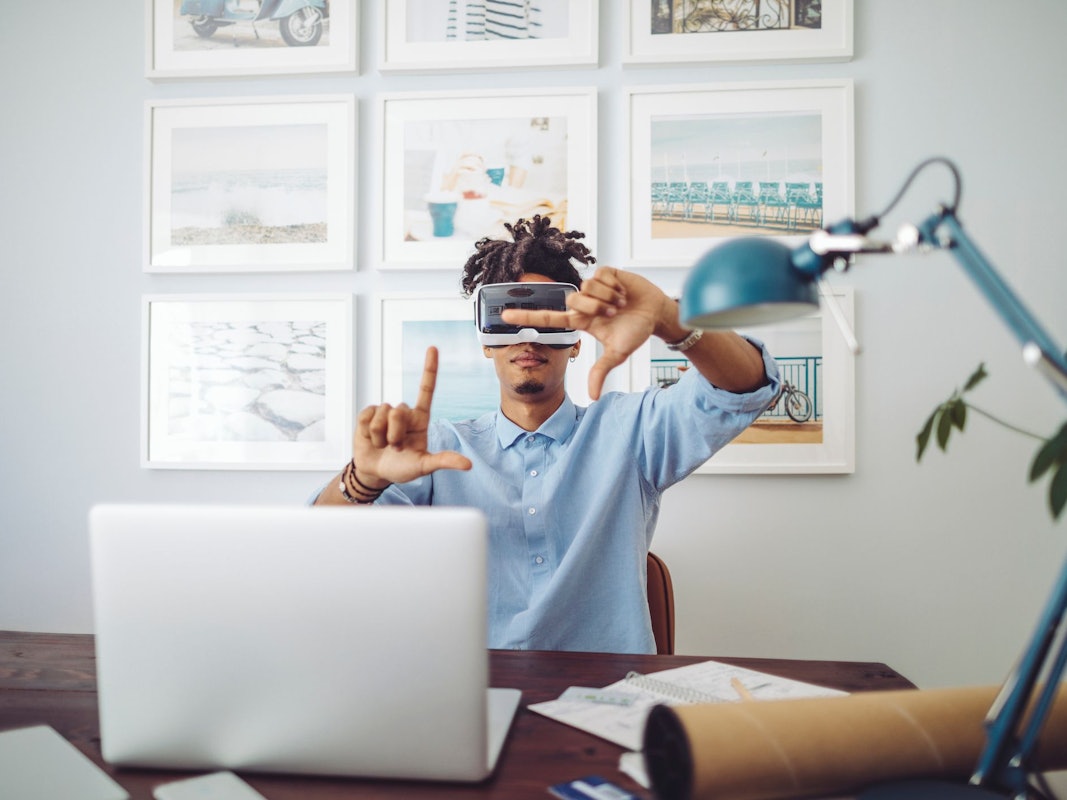 Mann sitzt am Schreibtisch vorm Laptop mit Virtual Reality Brille.