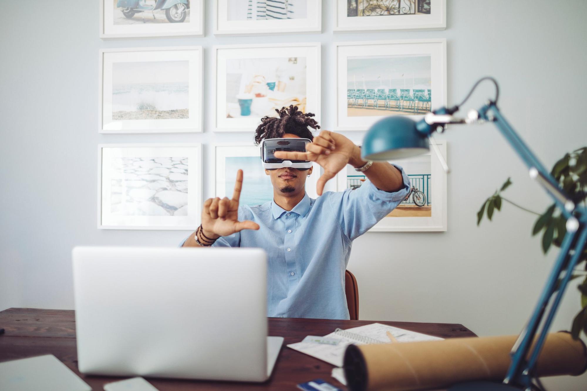 Mann sitzt am Schreibtisch vorm Laptop mit Virtual Reality Brille.