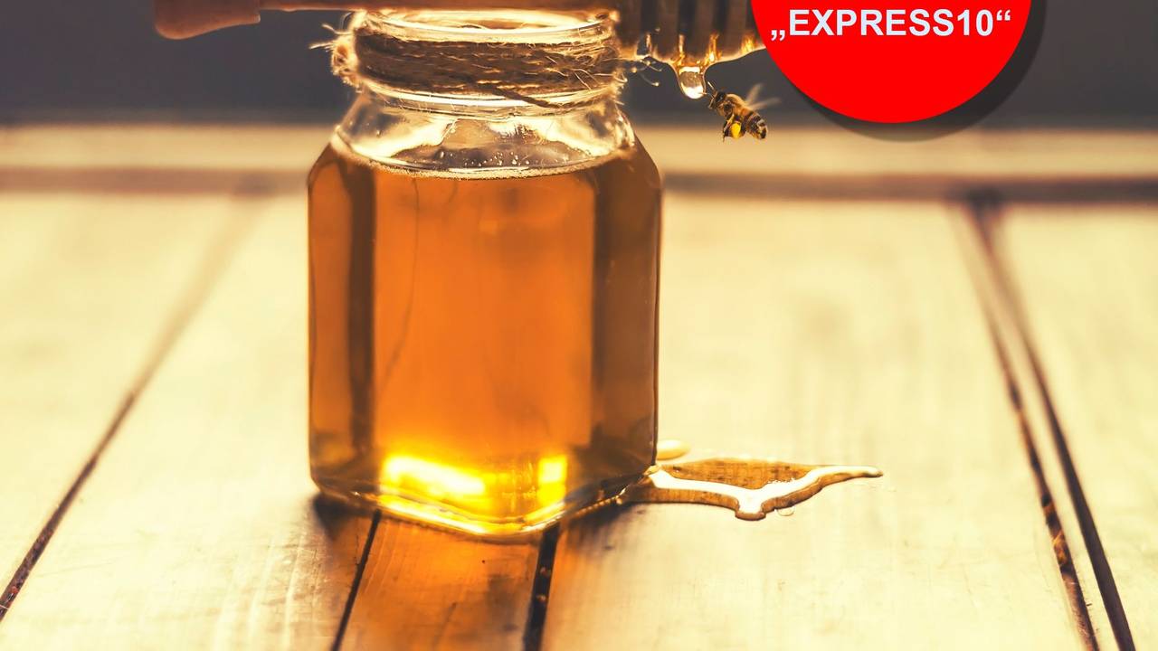 Indoor shot of a jar of honey with honey dripping from a honey dripper and flying bees