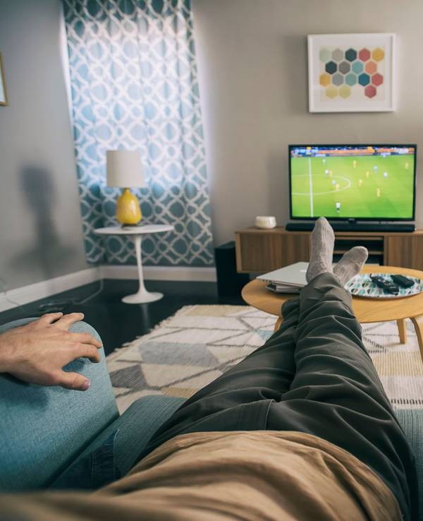 Auf dem Foto sitzt ein Mann auf einem Sessel und schaut Fußball auf einem kleinen Fernseher.