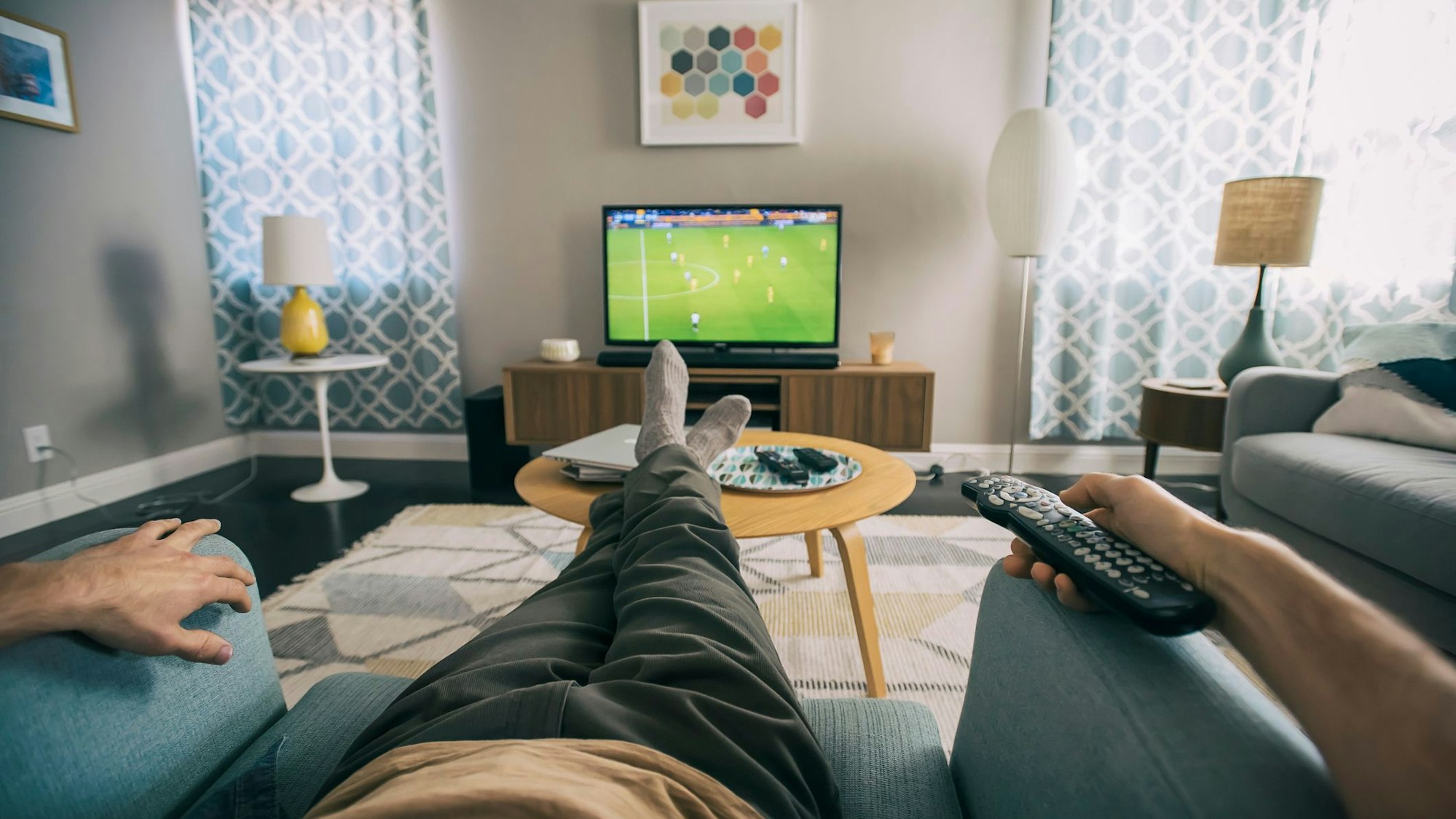 Auf dem Foto sitzt ein Mann auf einem Sessel und schaut Fußball auf einem kleinen Fernseher.