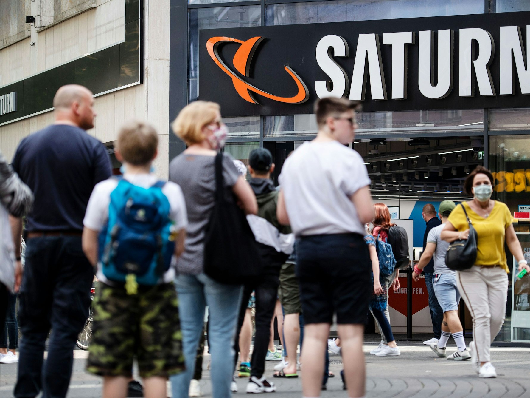 Menschen stehen in einer Warteschlange vor einer Filiale des Elektrohändlers Saturn an.